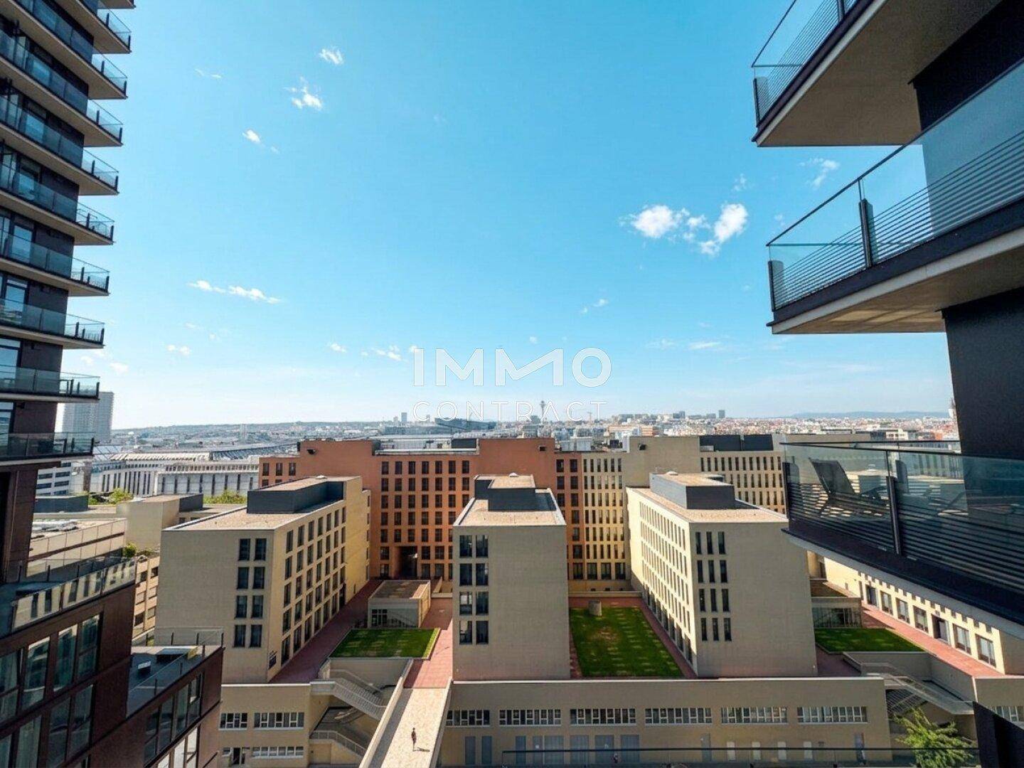 Panoramablick von oben auf begrünte Innenhöfe und moderne Gebäude mit Stadtpanorama im Hintergrund.
