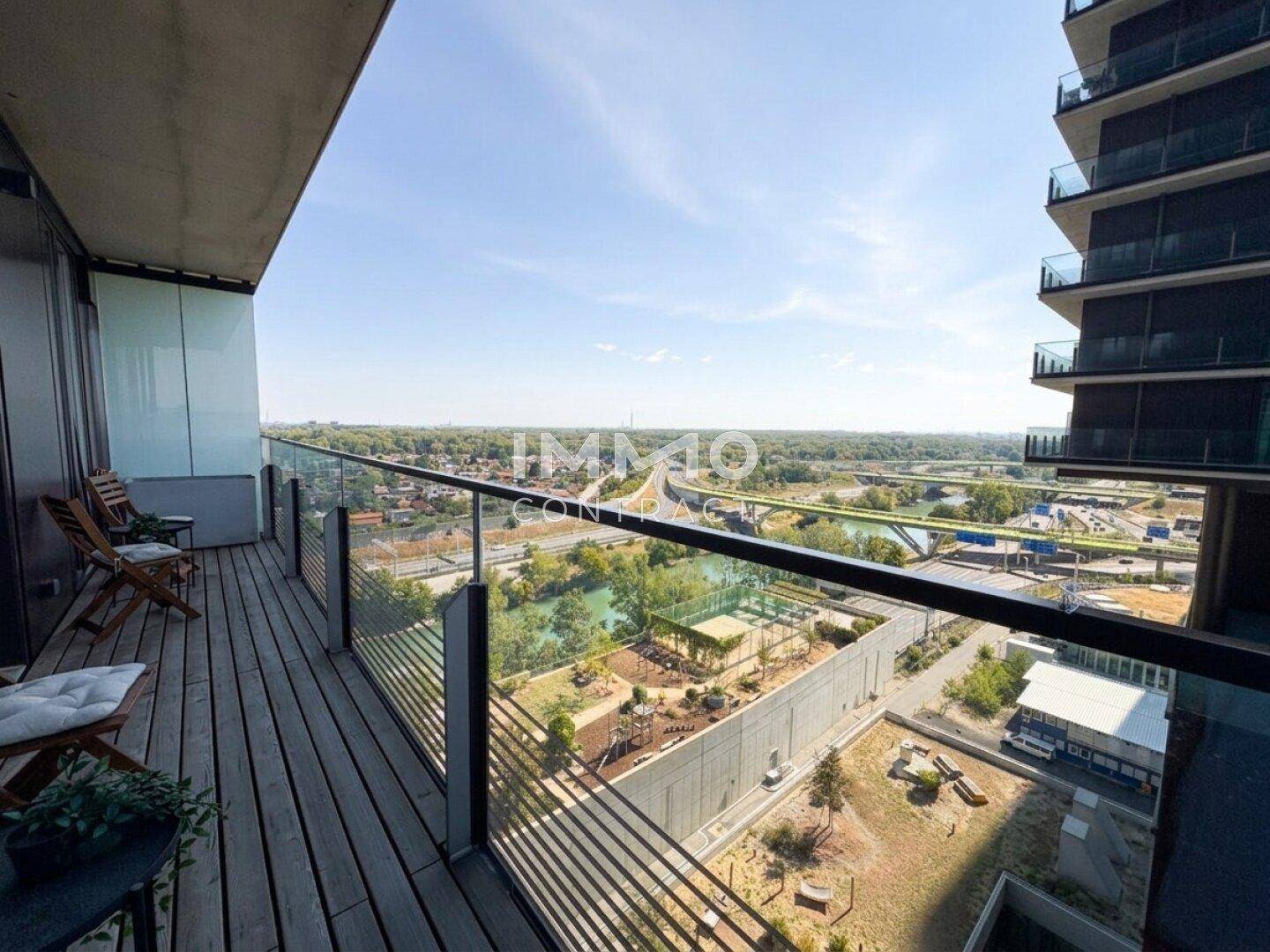 Geräumiger Balkon mit Holzdeck und Glasgeländer bietet weiten Blick über Fluss und Grünflächen.
