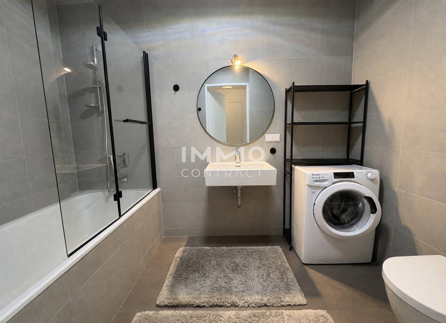 Modernes Badezimmer mit grauen Fliesen, Badewanne mit Duschwand und Waschmaschine.