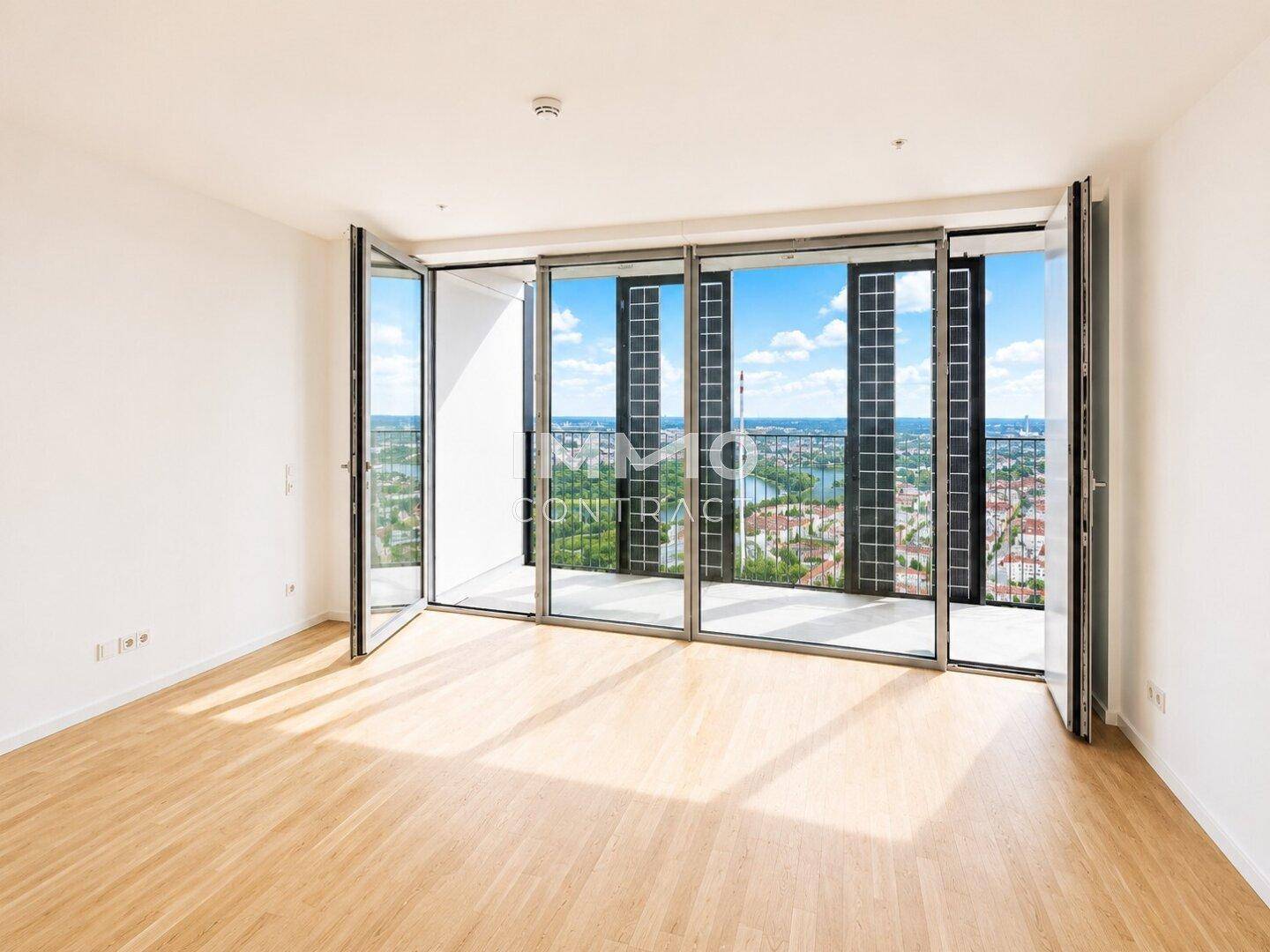 Lichtdurchfluteter Raum mit Holzboden und Zugang zu einem Balkon mit Panoramablick über die Stadt.