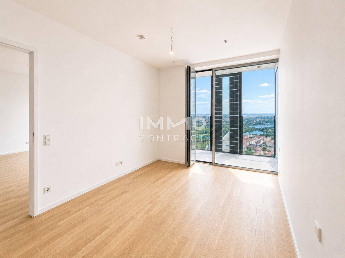Lichtdurchfluteter Raum mit Holzboden und großen Fenstern, die einen Panoramablick auf die Stadt ermöglichen.