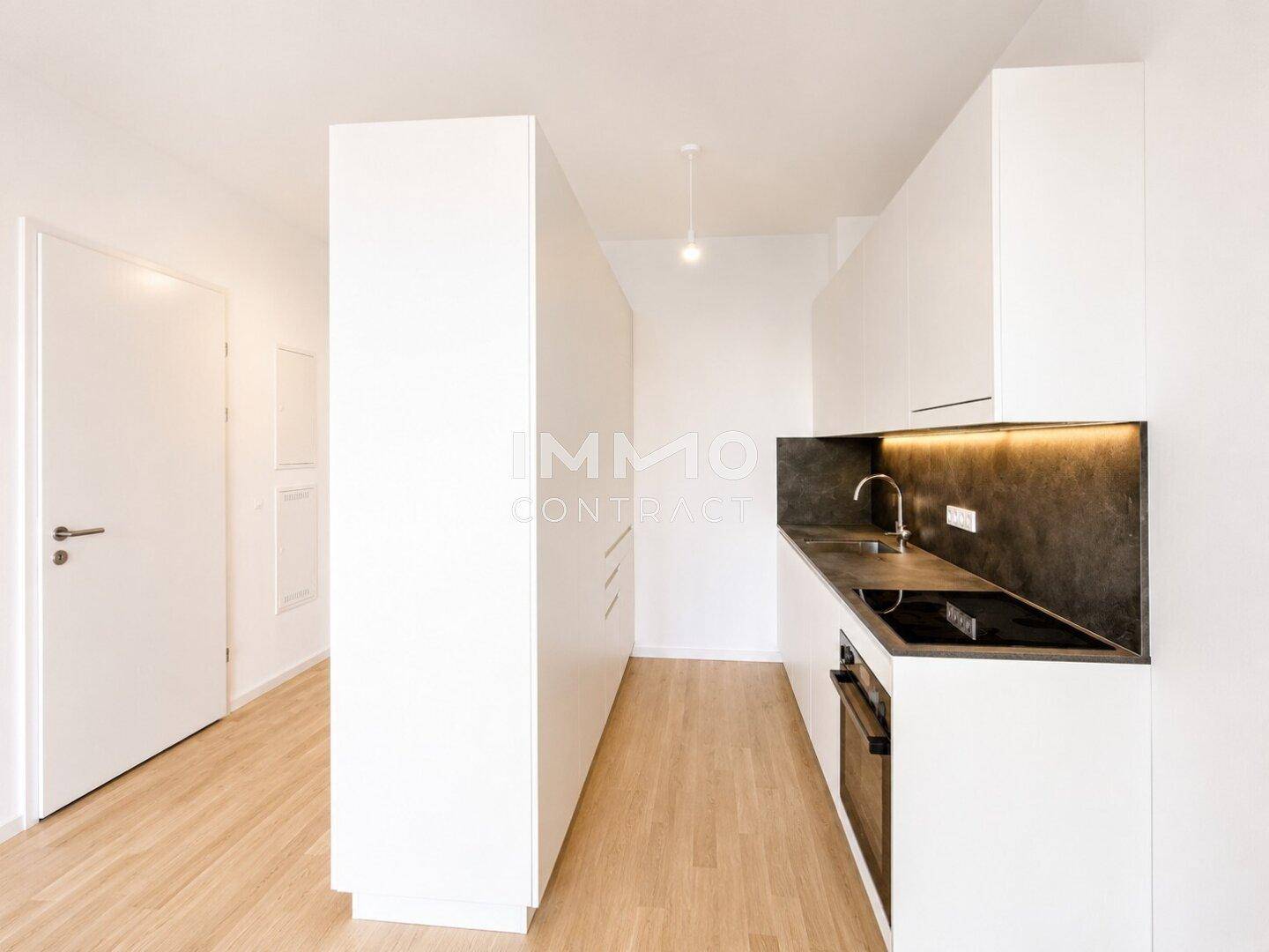 Moderne, kompakte Küchenzeile mit weißen Schränken, dunkler Arbeitsplatte und Holzboden.