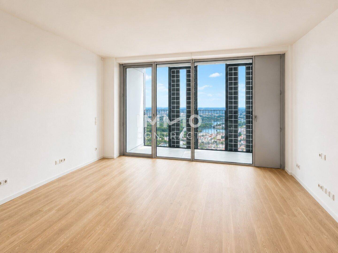 Geräumiges, unmöbliertes Zimmer mit Holzboden und breiter Fensterfront mit Stadt- und Flussblick.