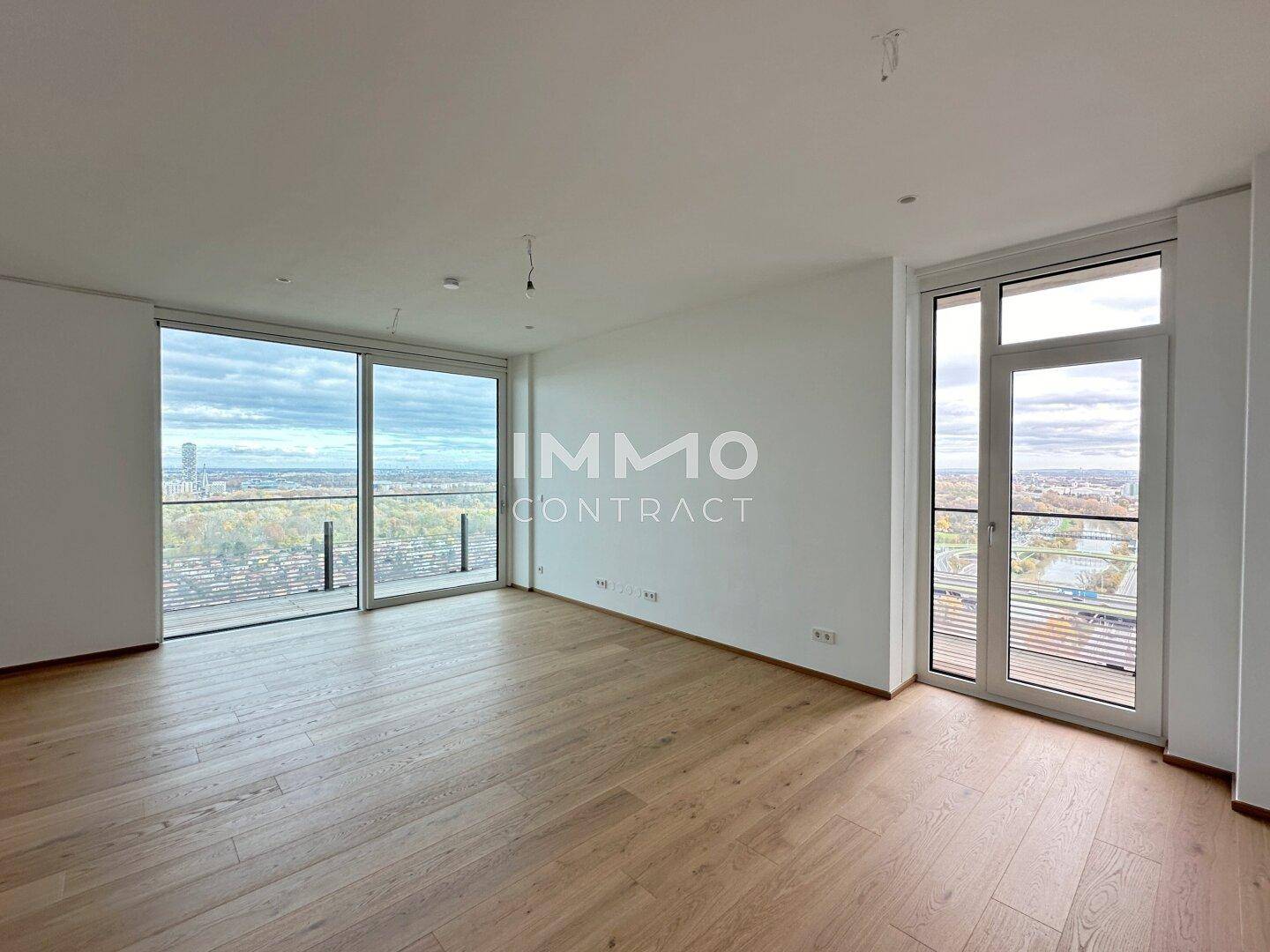 Geräumiges, leeres Wohnzimmer mit großen Fenstern und hellem Holzparkett.