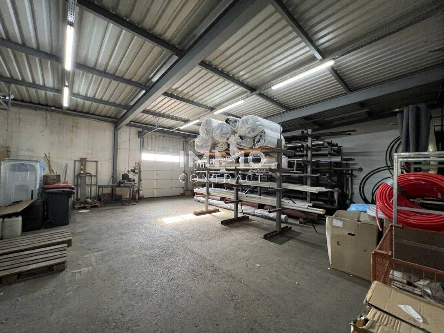 Geräumige Lagerhalle mit hohen Decken, Betonboden und Rolltor, ideal für die Lagerung von Materialien.