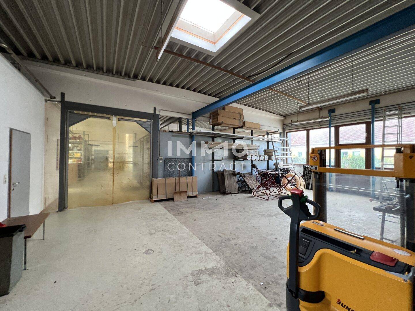 Lagerhalle mit hohen Decken, Oberlicht und einem Rolltor, ausgestattet mit einem Hubwagen für den Transport.