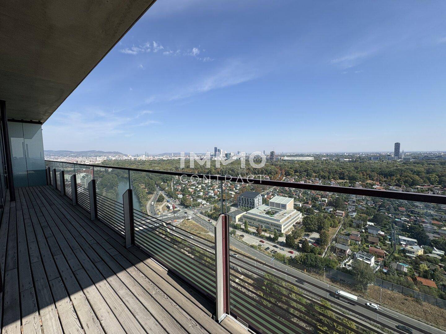 Langer Balkon mit Holzbelag und Glasgeländer bietet einen weiten Blick über die Stadt.