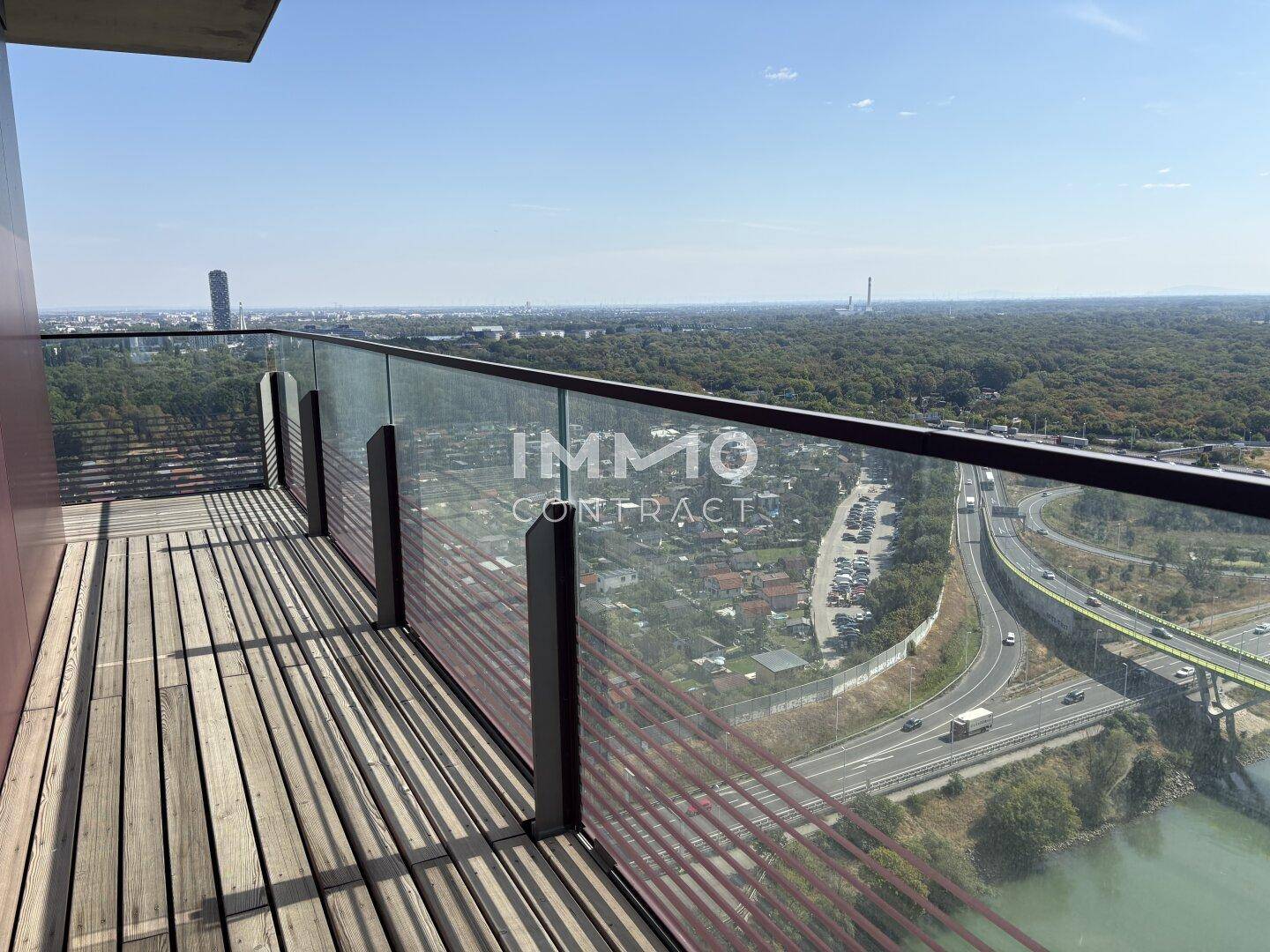 Geräumiger Balkon mit Holzbelag und Glasgeländer bietet einen weiten Stadtblick.