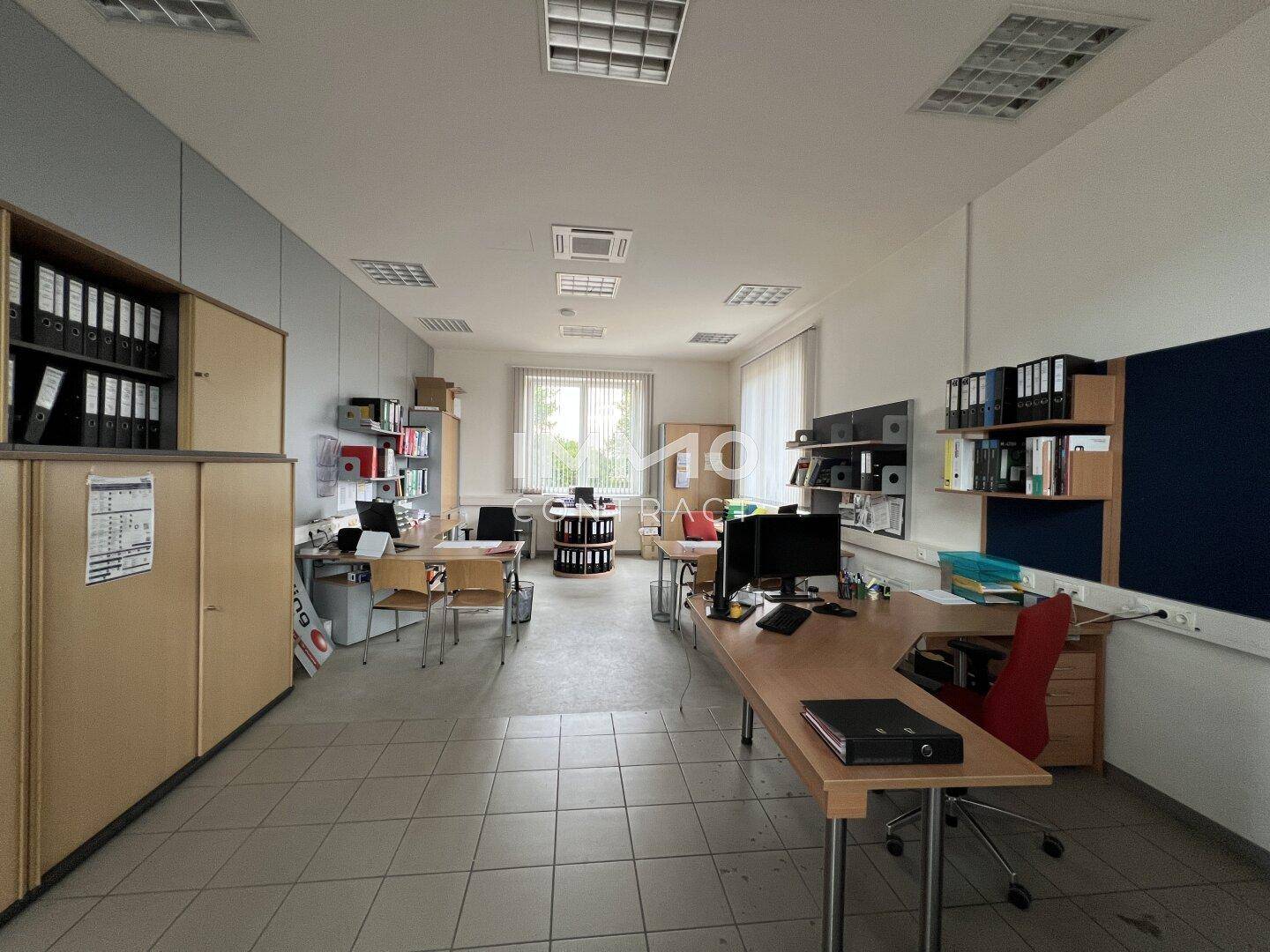Helles Büro mit mehreren Arbeitsplätzen, Fliesenboden und großen Fenstern, ideal für ein Team.