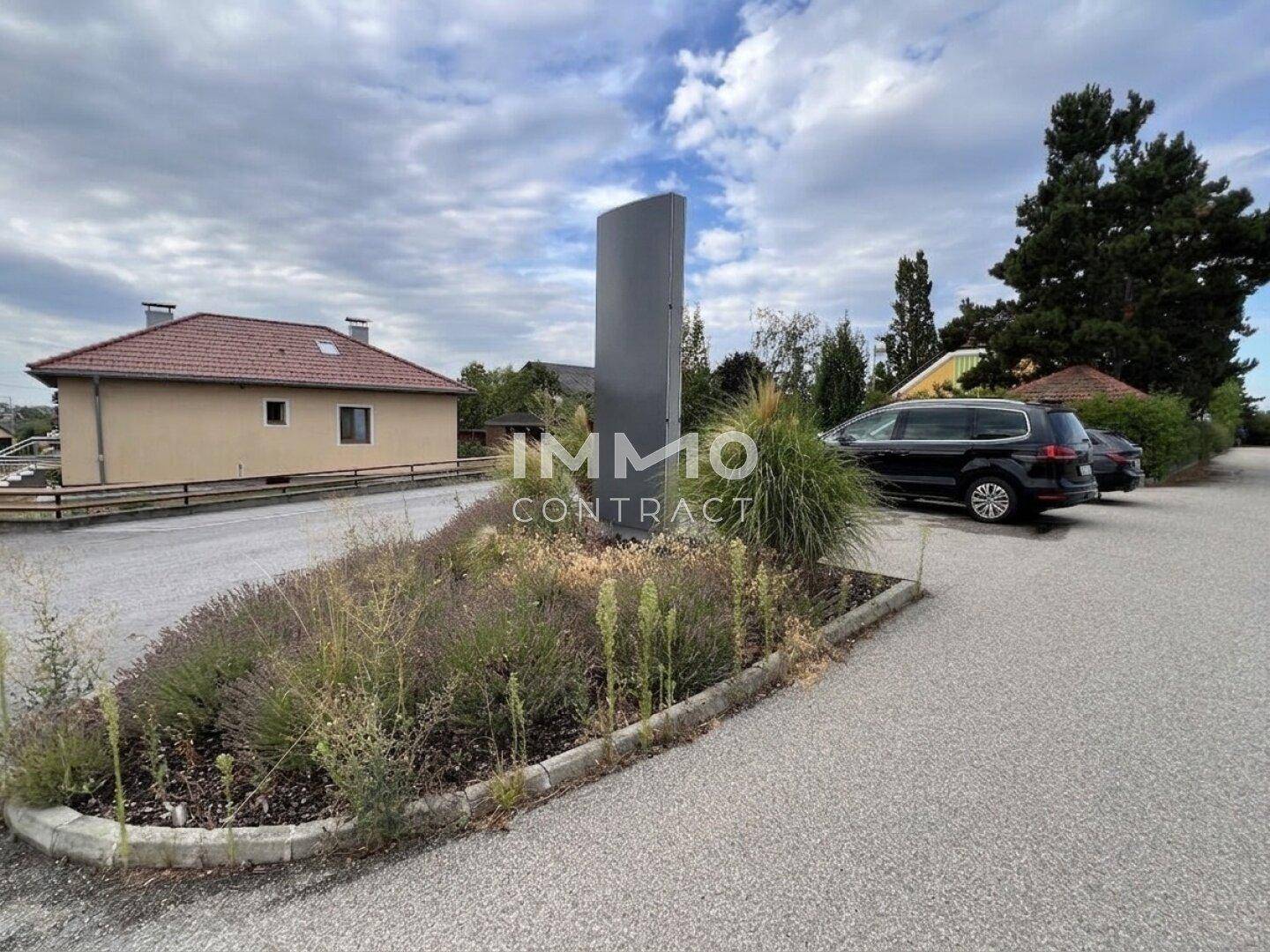 Parkplatzbereich mit dekorativer Bepflanzung und einem modernen Werbepylon.