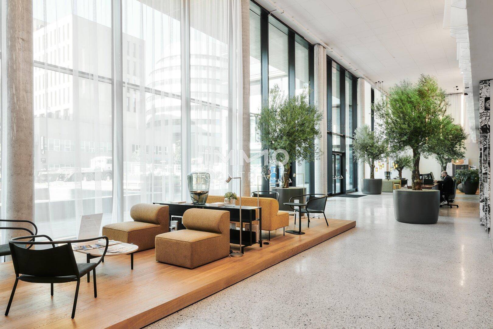 Helle und geräumige Lobby mit großen Fenstern, bequemen Sitzgelegenheiten und Pflanzen.