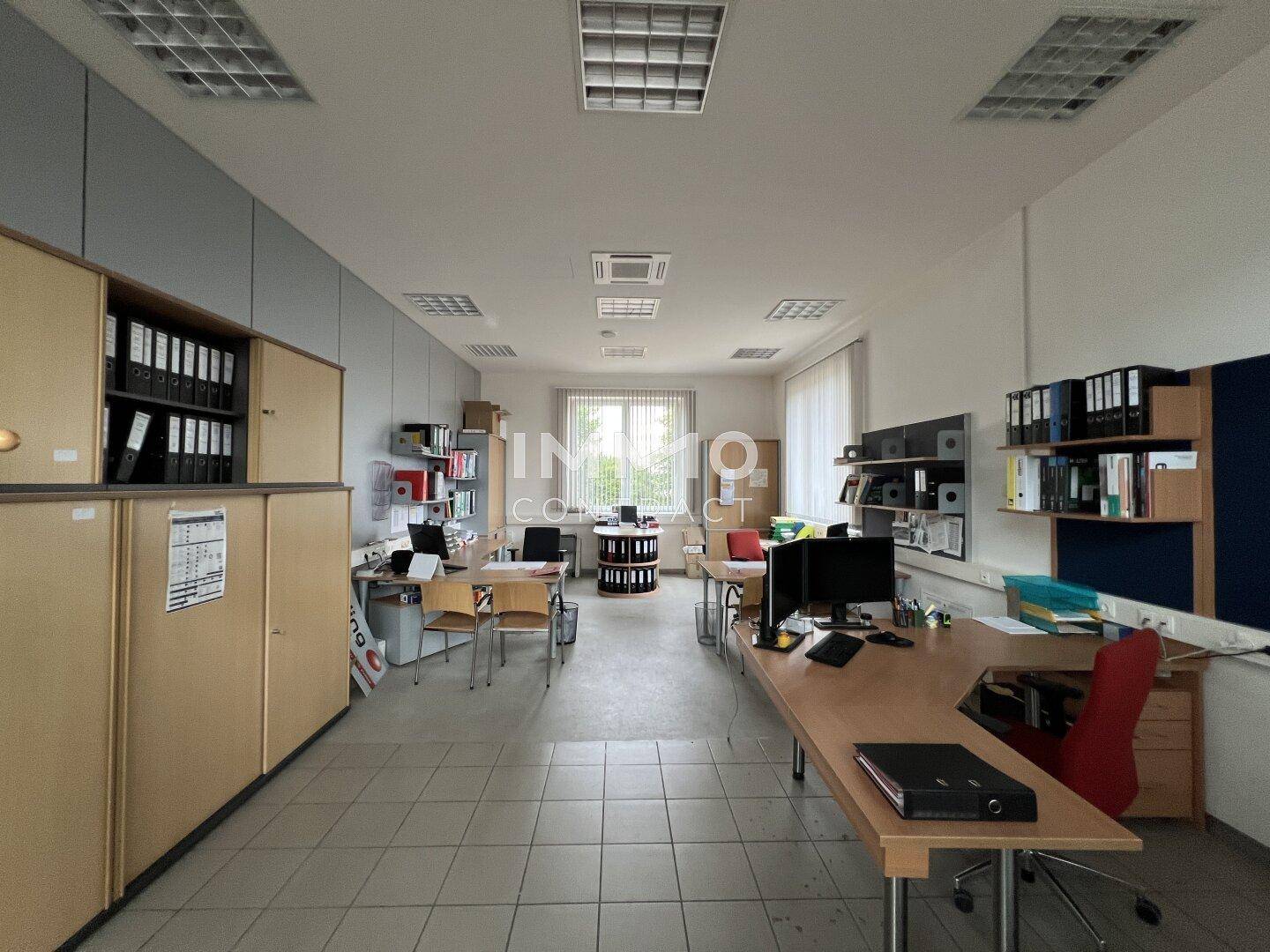 Geräumiges Büro mit mehreren Arbeitsplätzen, Aktenschränken und natürlichem Lichteinfall.