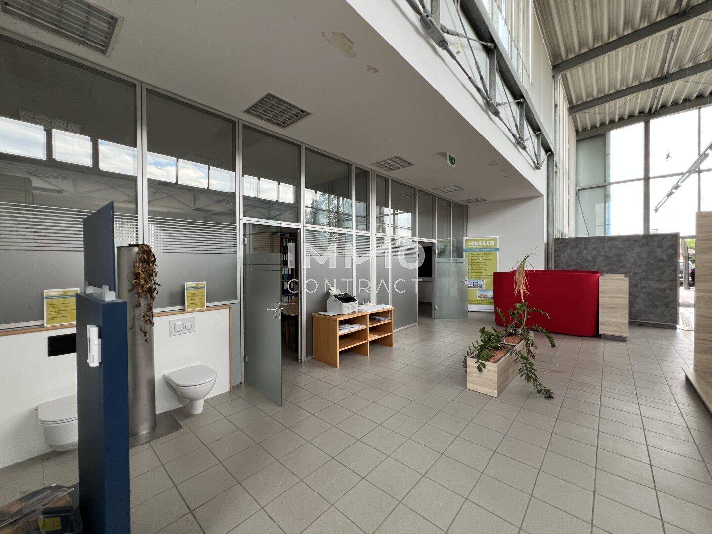 Offener Gewerbebereich mit Fliesenboden, Glaswänden und sichtbaren Toiletten, hell und funktional.