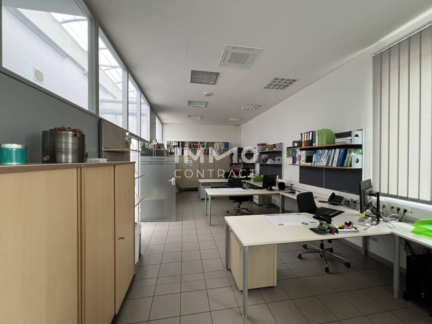 Helles Büro mit langen Fensterfronten, Fliesenboden und mehreren Arbeitsplätzen, ideal für Teamarbeit.