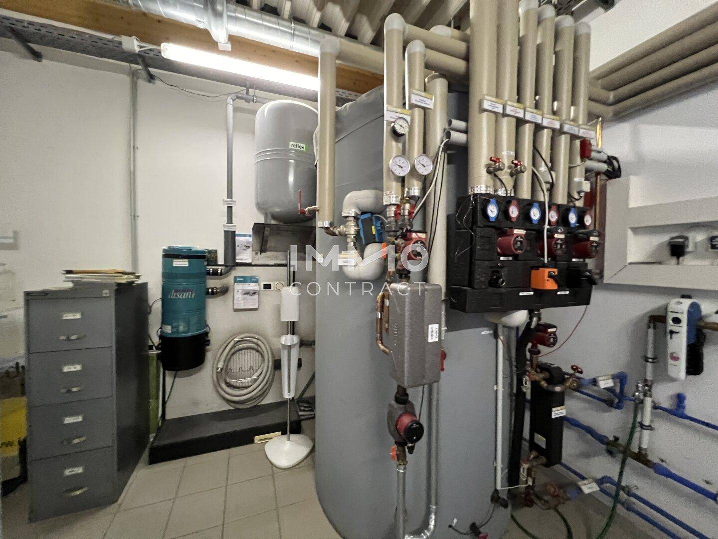 Heizungsraum mit großem Warmwasserspeicher, Pumpen und umfangreicher Verrohrung.