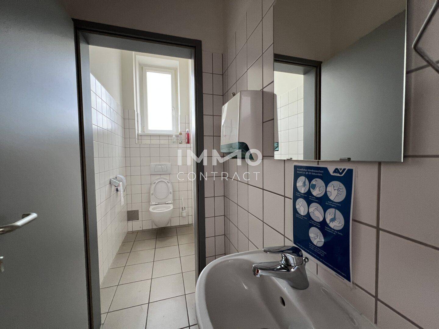 Toilettenraum mit WC, Waschbecken und Fenster, ausgestattet mit weißen Fliesen.
