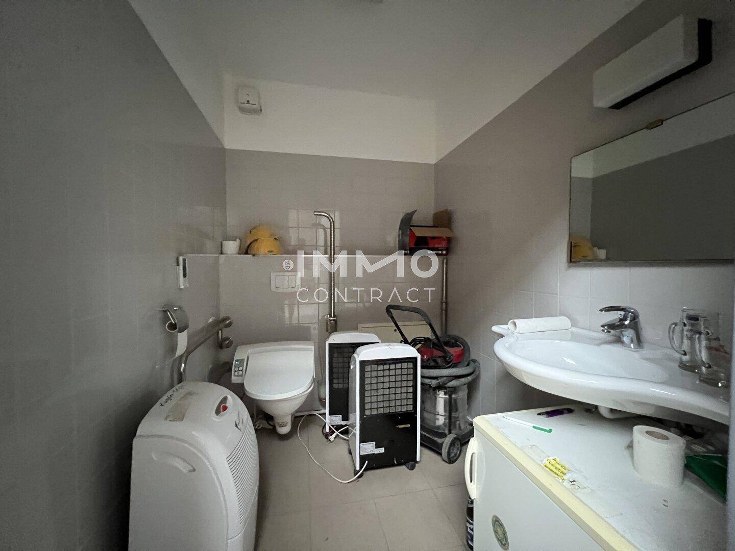 Geräumiges Badezimmer mit Waschbecken, Toilette und grauen Fliesen, derzeit als Abstellraum genutzt.