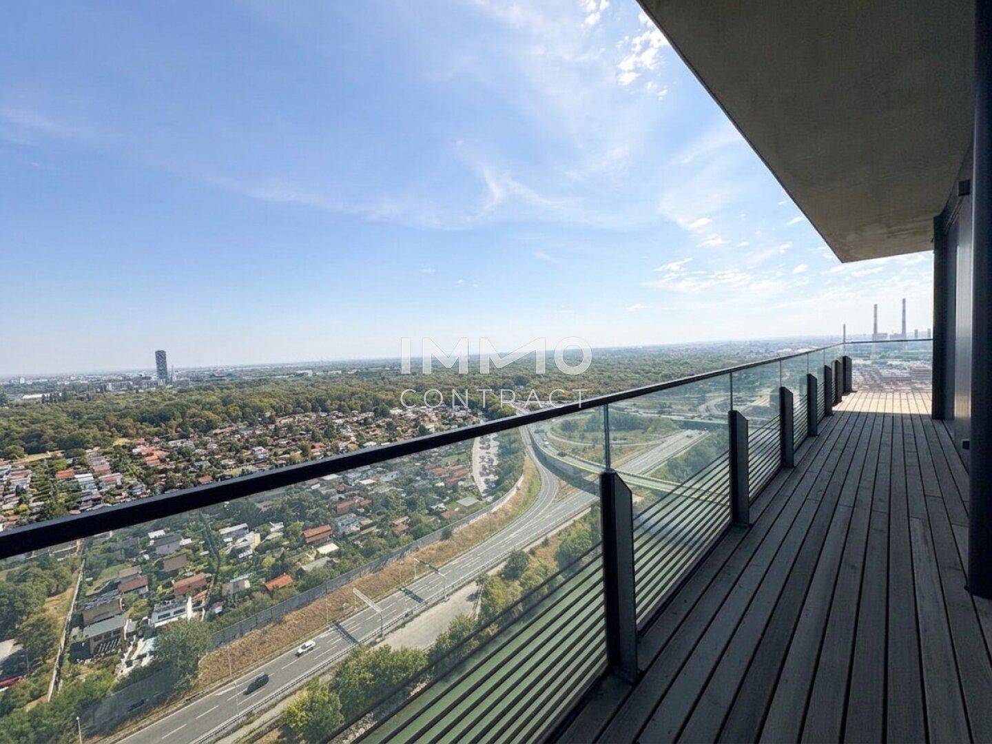 Breiter Balkon mit Holzbelag und Glasgeländer bietet einen weiten Blick über die Stadt.