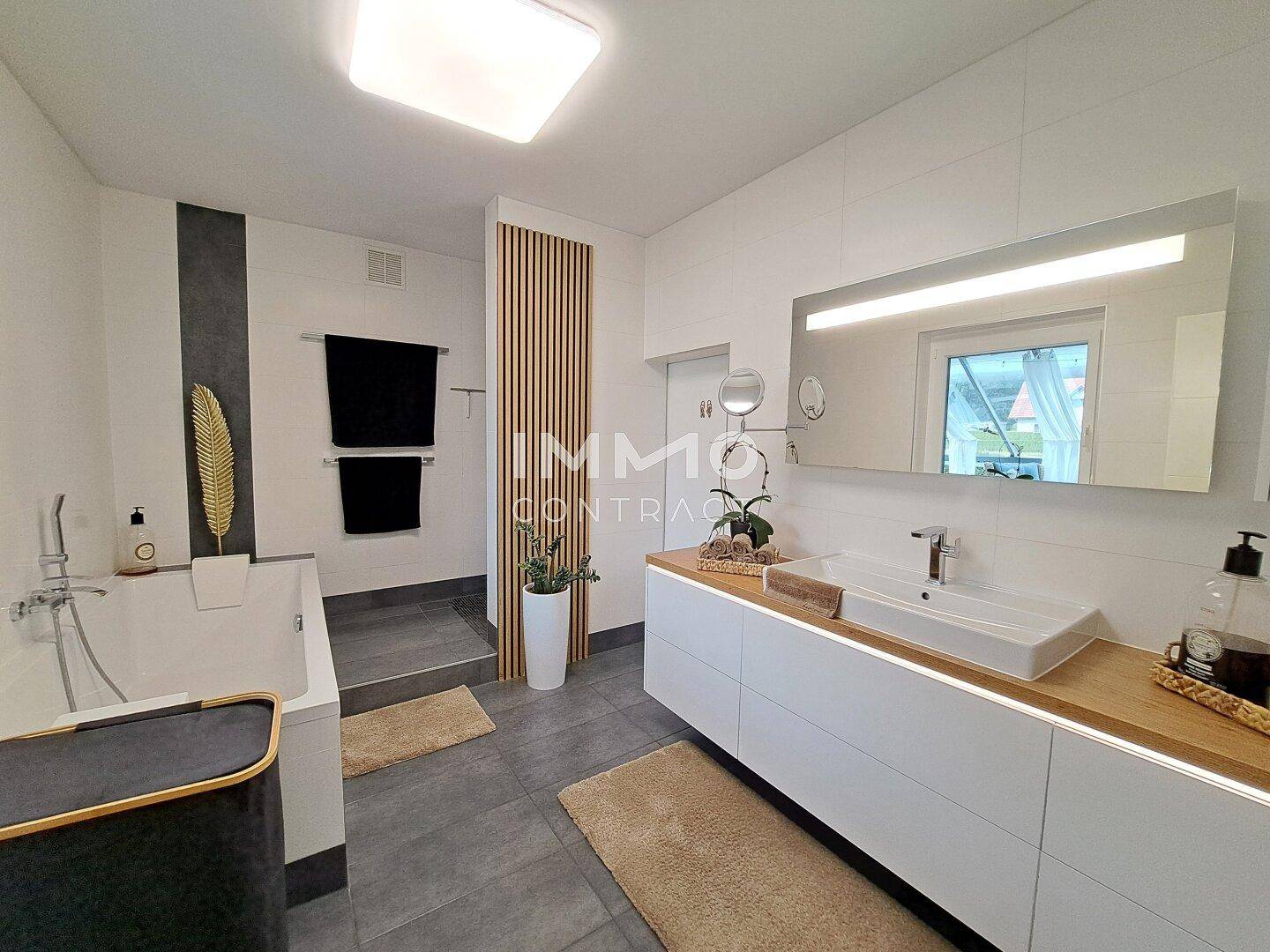 Modernes Badezimmer mit Badewanne, großem Waschtisch und dunklen Fliesen.