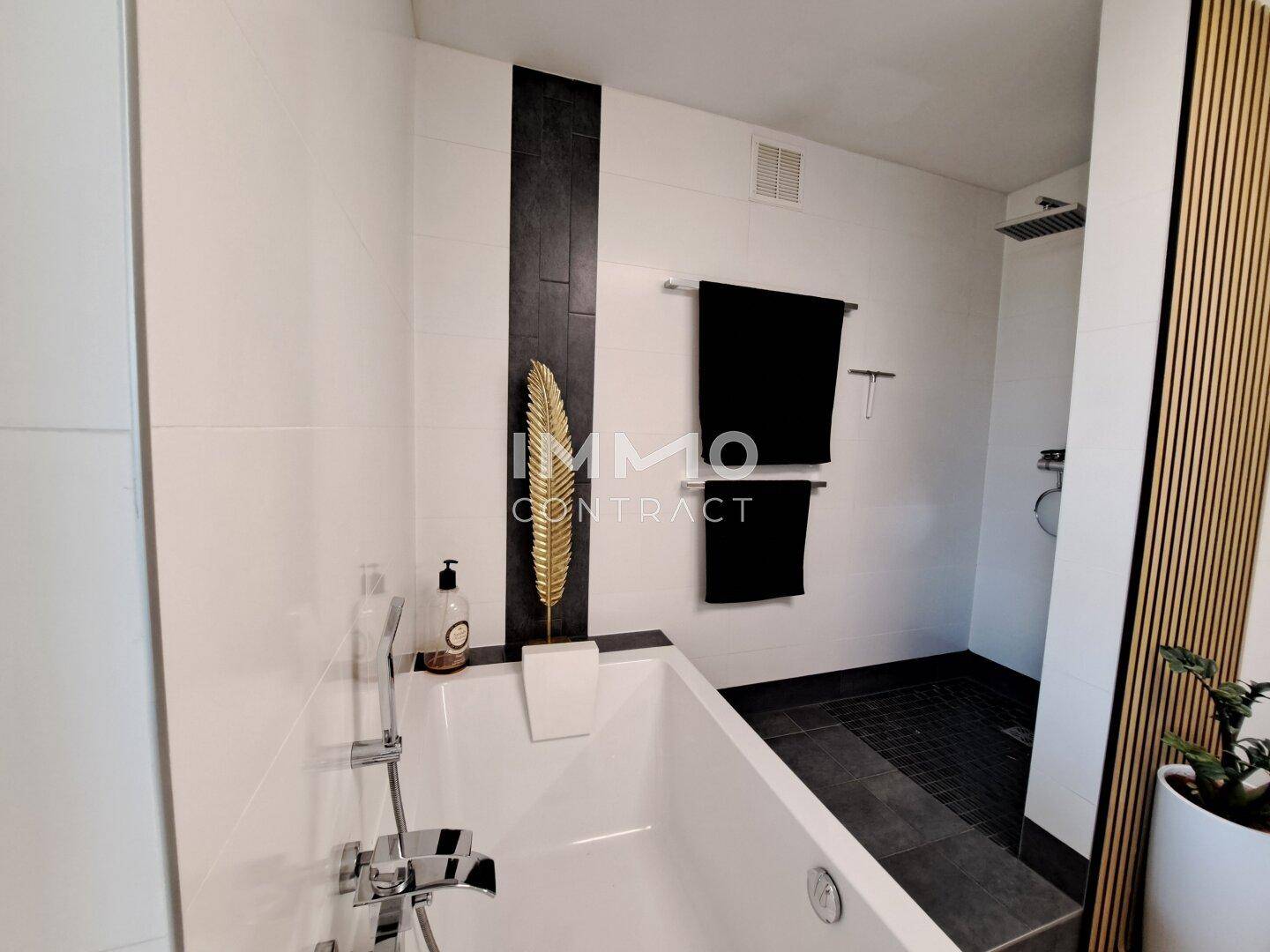 Elegantes Badezimmer mit Badewanne, begehbarer Dusche und dunklen Akzenten.