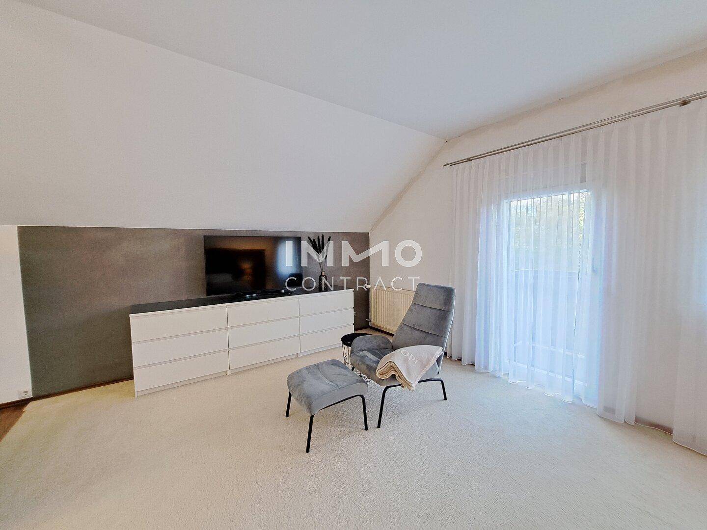 Helles Schlafzimmer mit Sessel, Kommode und Zugang zu einem Balkon.