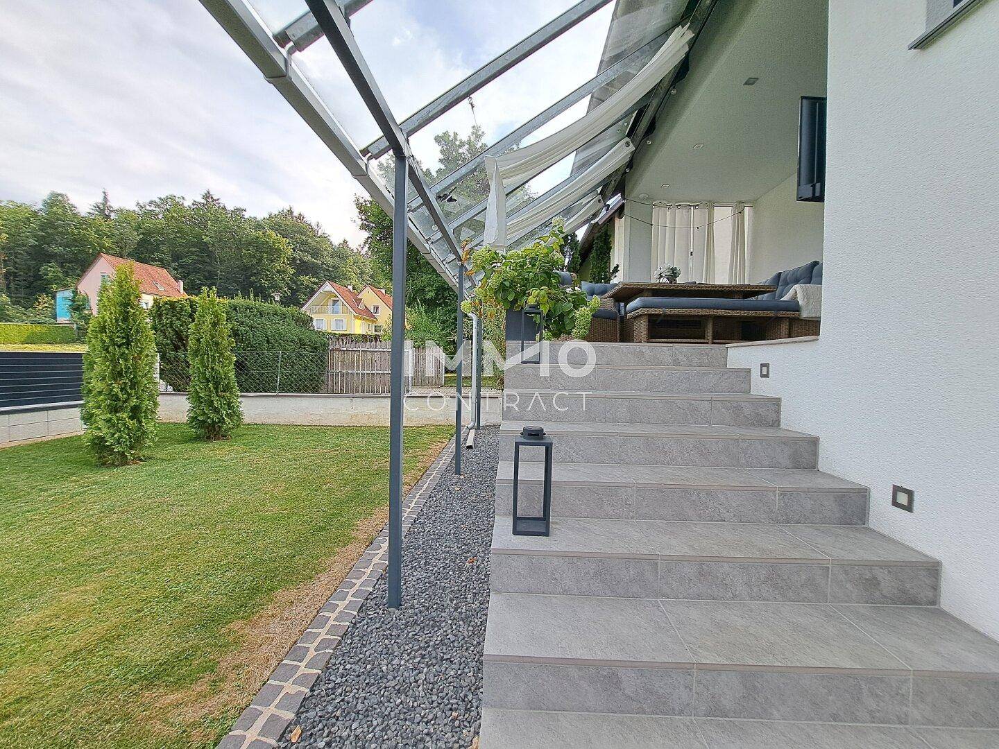 Elegante Steintreppe führt zur überdachten Terrasse mit Gartenblick.
