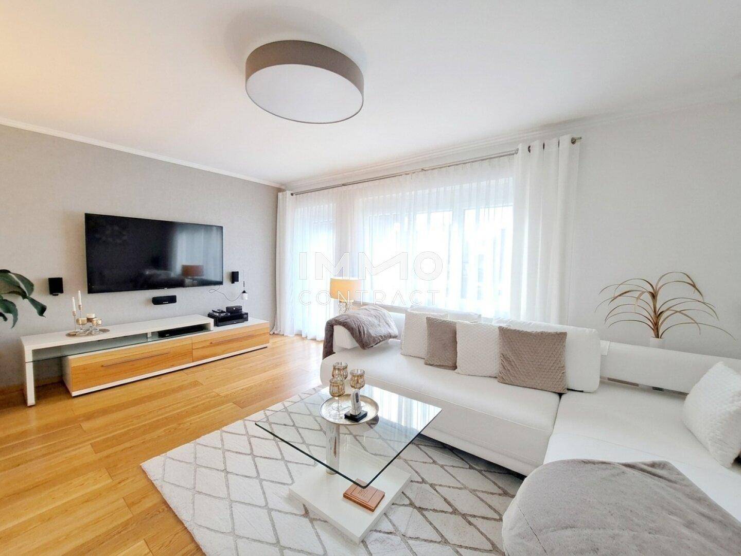 Helles Wohnzimmer mit modernem Sofa, Holzboden und großem Fernseher.