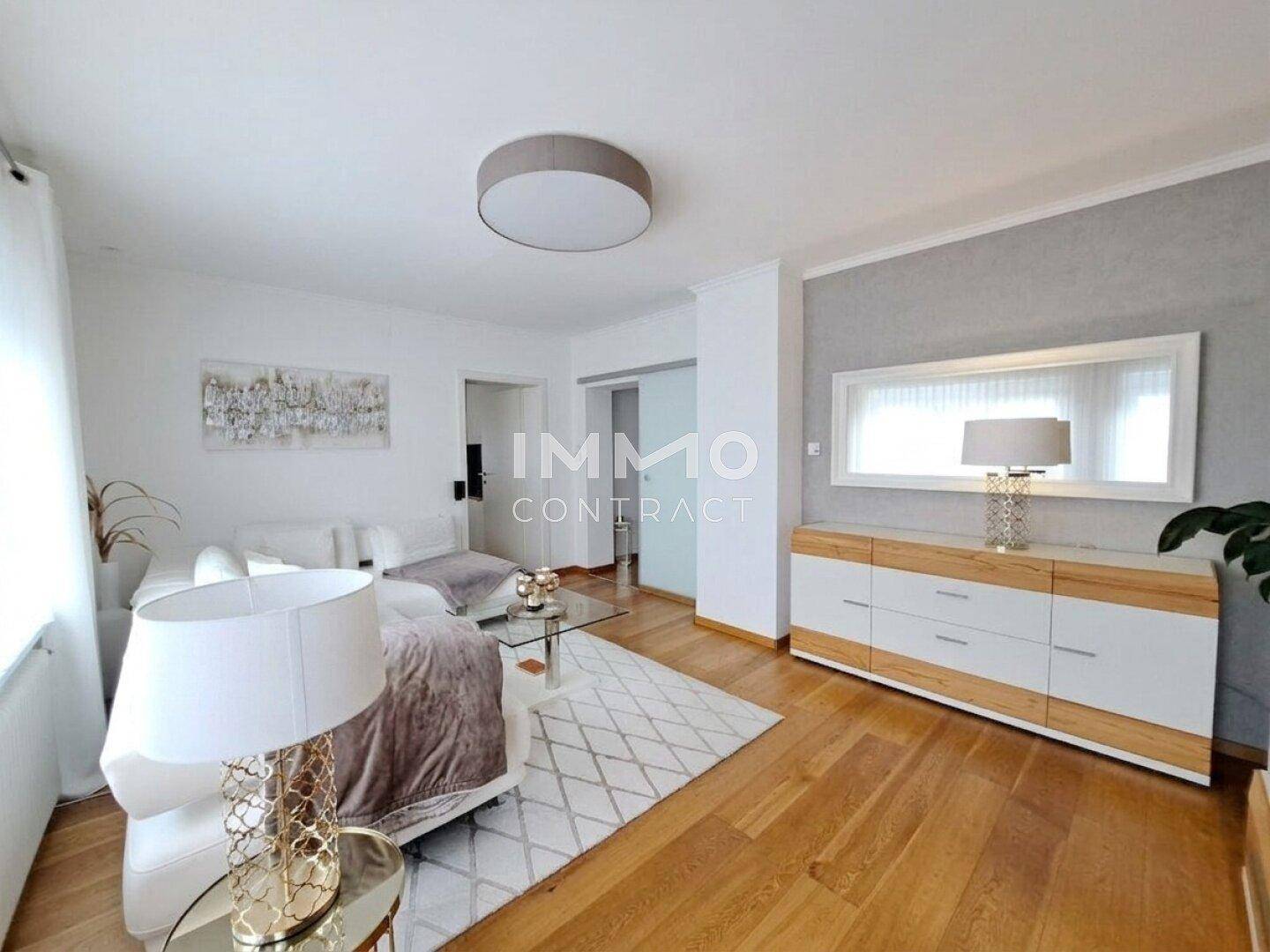 Geräumiges Wohnzimmer mit Holzboden, weißem Sofa und eleganter Kommode.