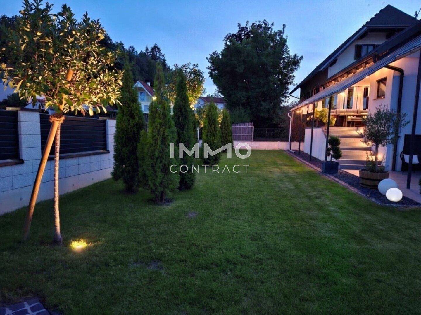 Gepflegter Gartenbereich bei Dämmerung mit Bäumen und stimmungsvoller Beleuchtung.