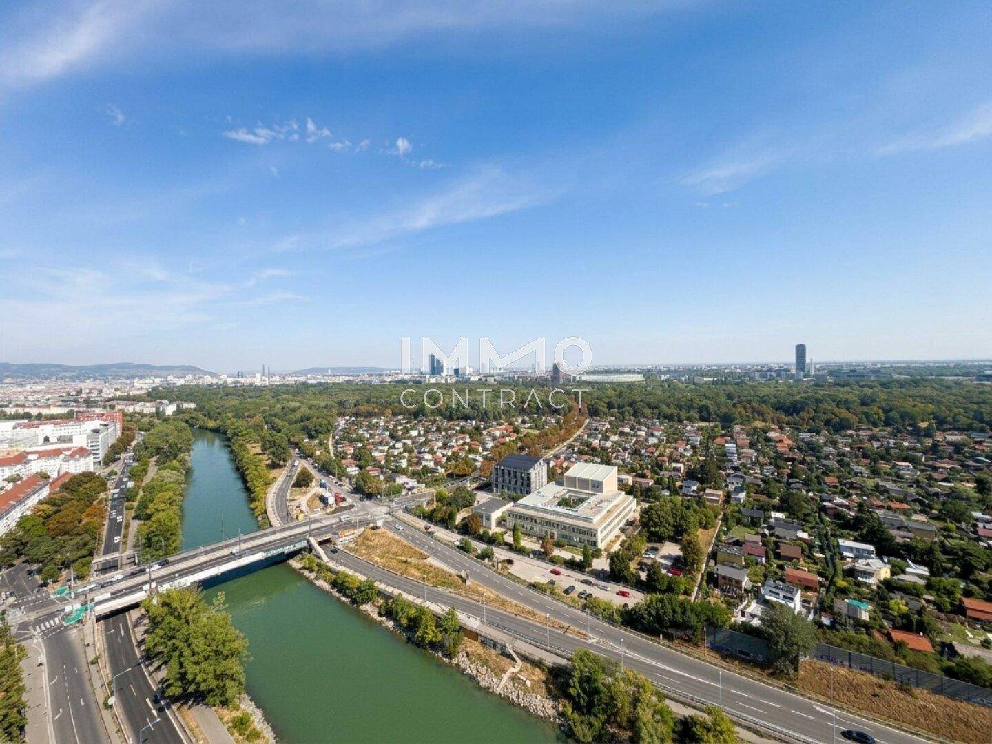Weitläufige Luftaufnahme der Stadt mit Fluss, Brücken und grünen Wohngebieten unter blauem Himmel.