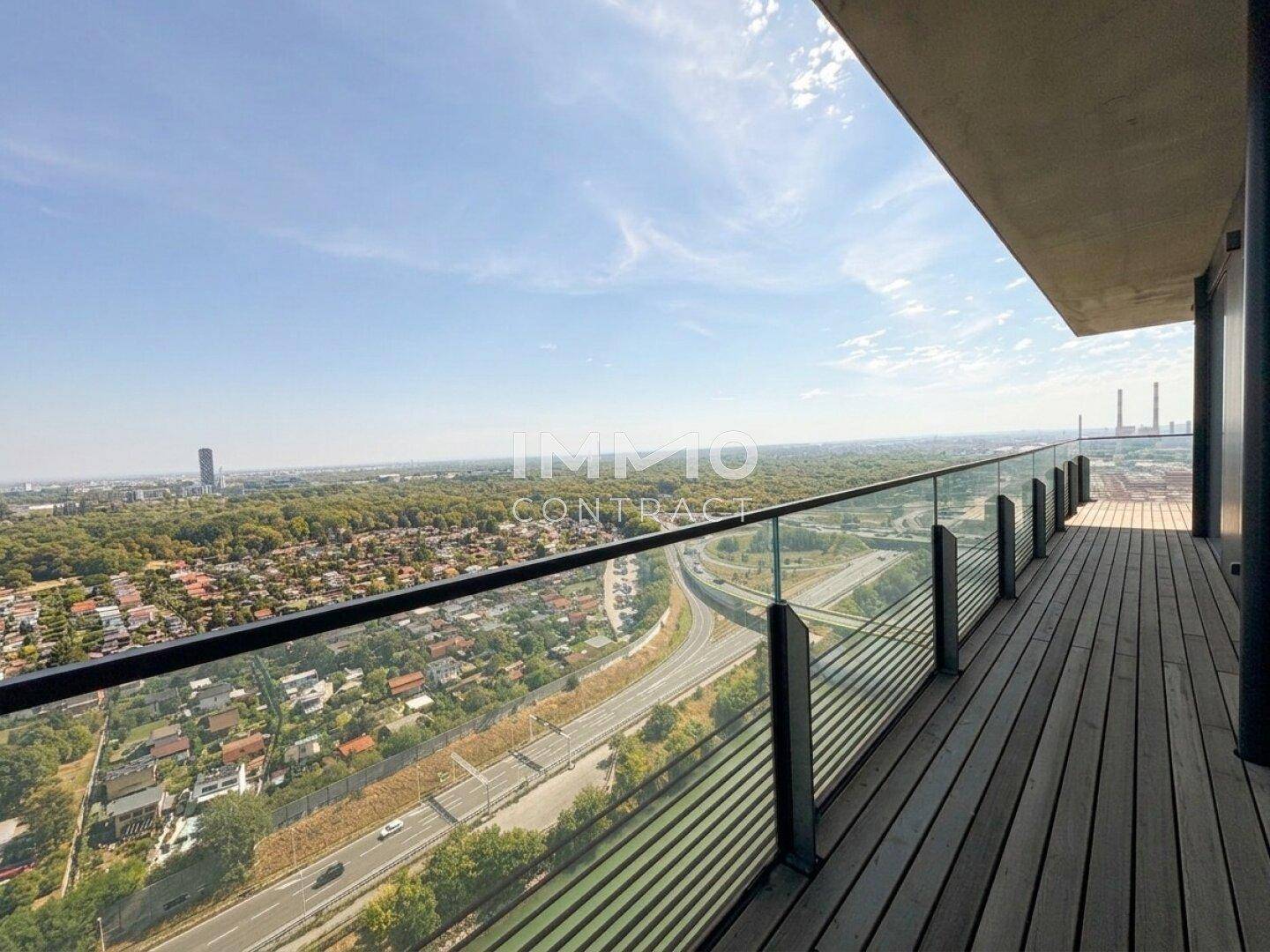 Geräumiger Balkon mit Holzbelag und Glasgeländer bietet weite Aussicht auf Autobahn und Grünflächen.