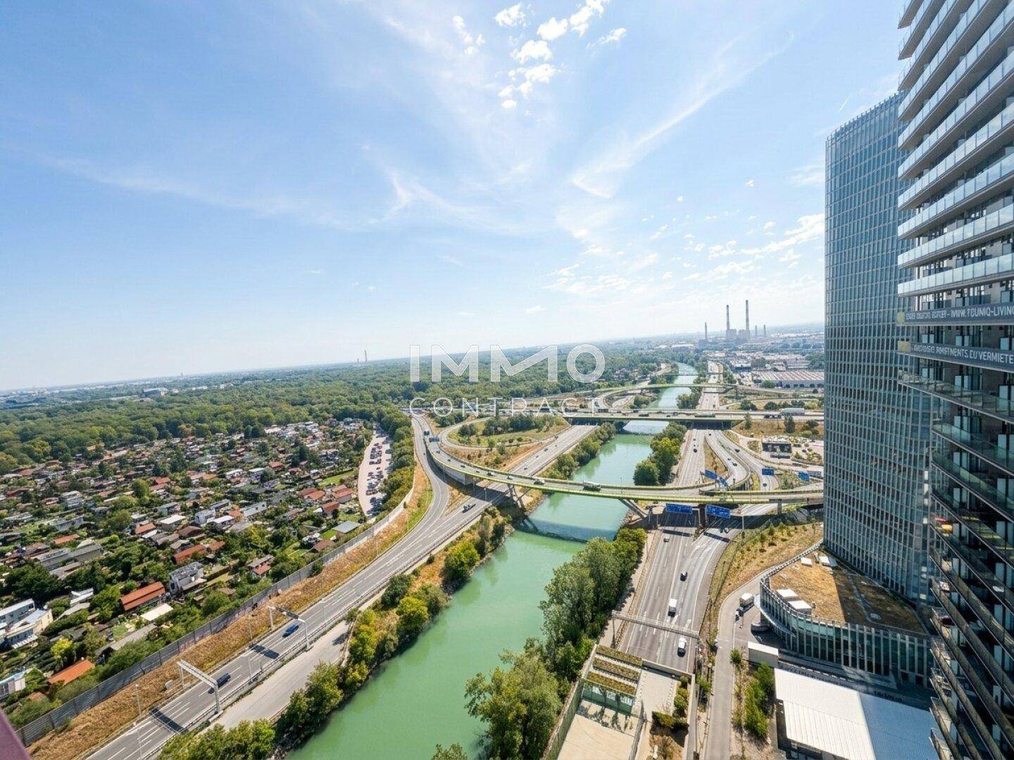Weitläufige Luftaufnahme der Stadt mit Fluss, Autobahn und einem modernen Hochhaus unter blauem Himmel.