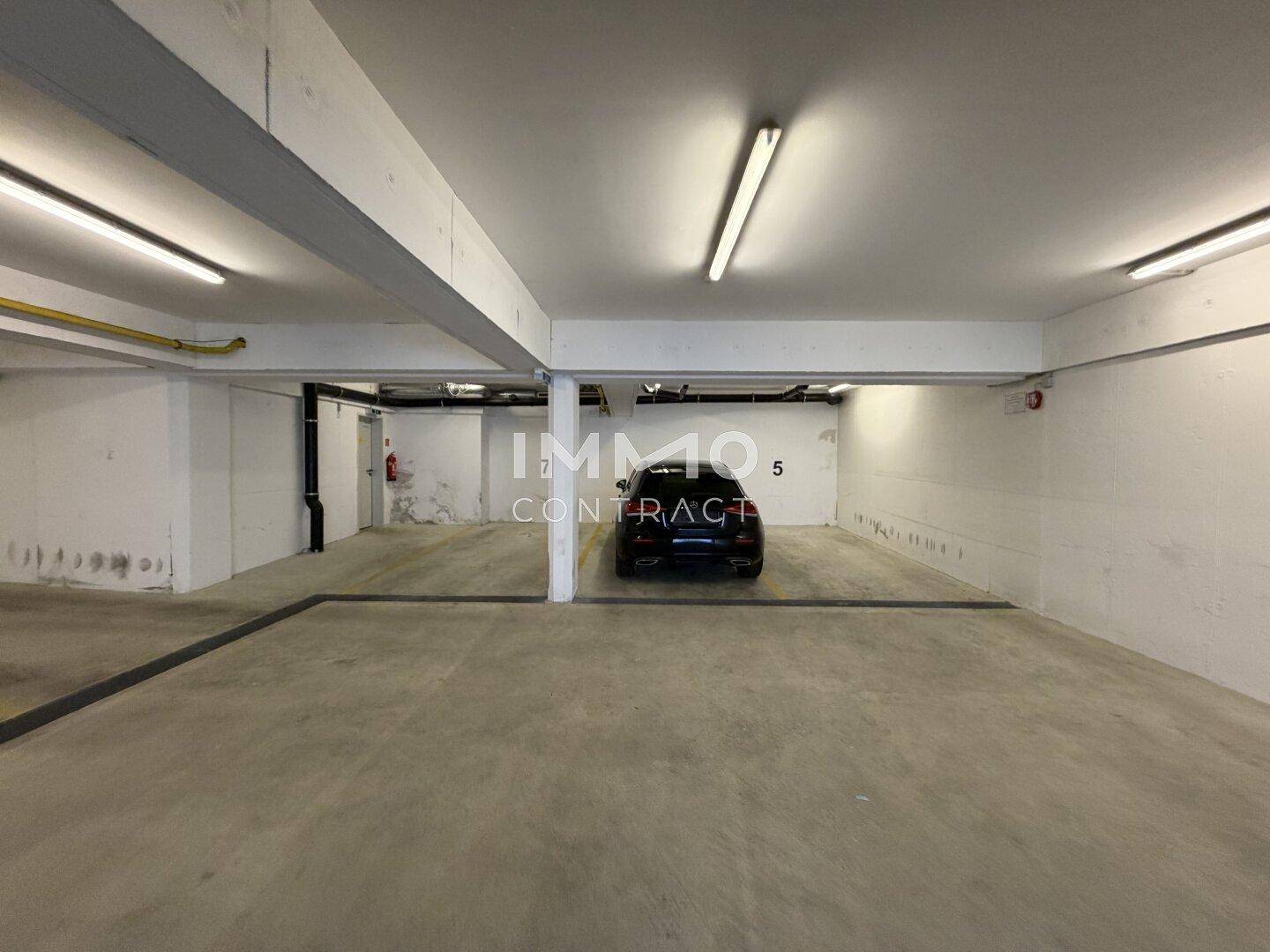 Geräumige Tiefgarage mit Betonboden, Deckenbeleuchtung und markierten Parkplätzen für Fahrzeuge.