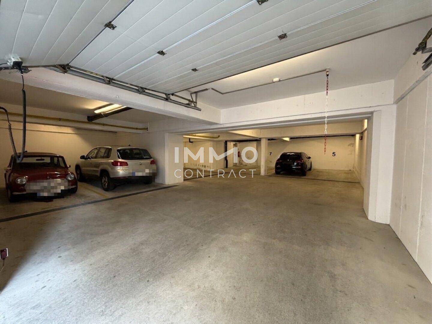Innenansicht einer Tiefgarage mit mehreren geparkten Fahrzeugen und heller Deckenbeleuchtung.