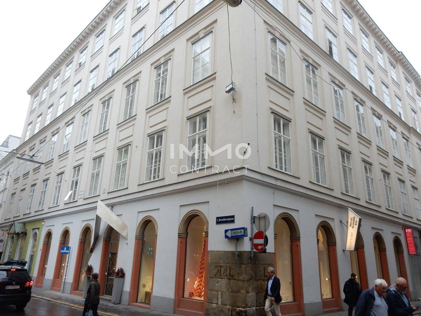 Historisches Eckgebäude mit vielen Fenstern und Geschäften im Erdgeschoss in einer städtischen Umgebung.