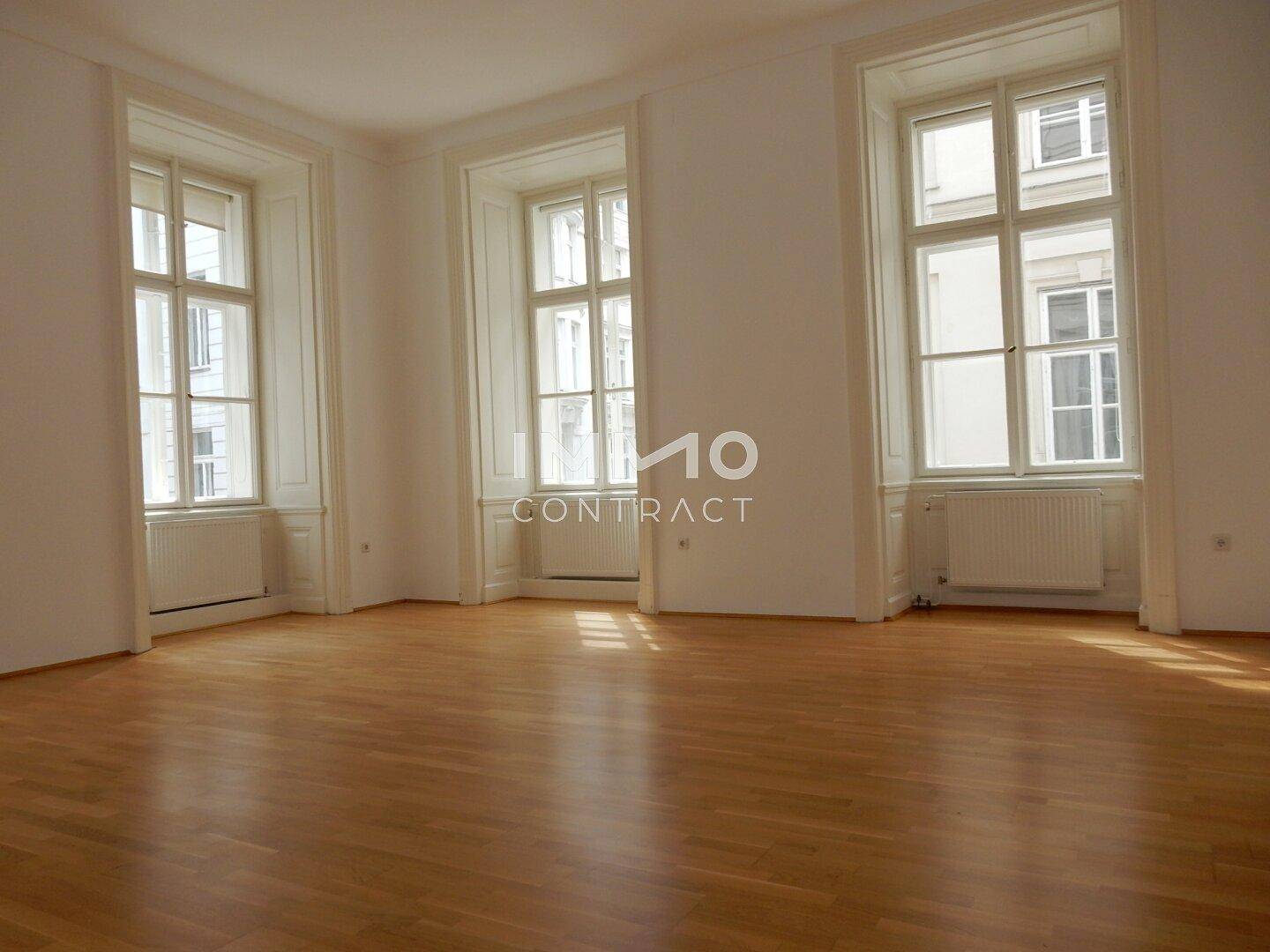 Heller, leerer Raum mit drei großen Fenstern, Parkettboden und viel natürlichem Licht.