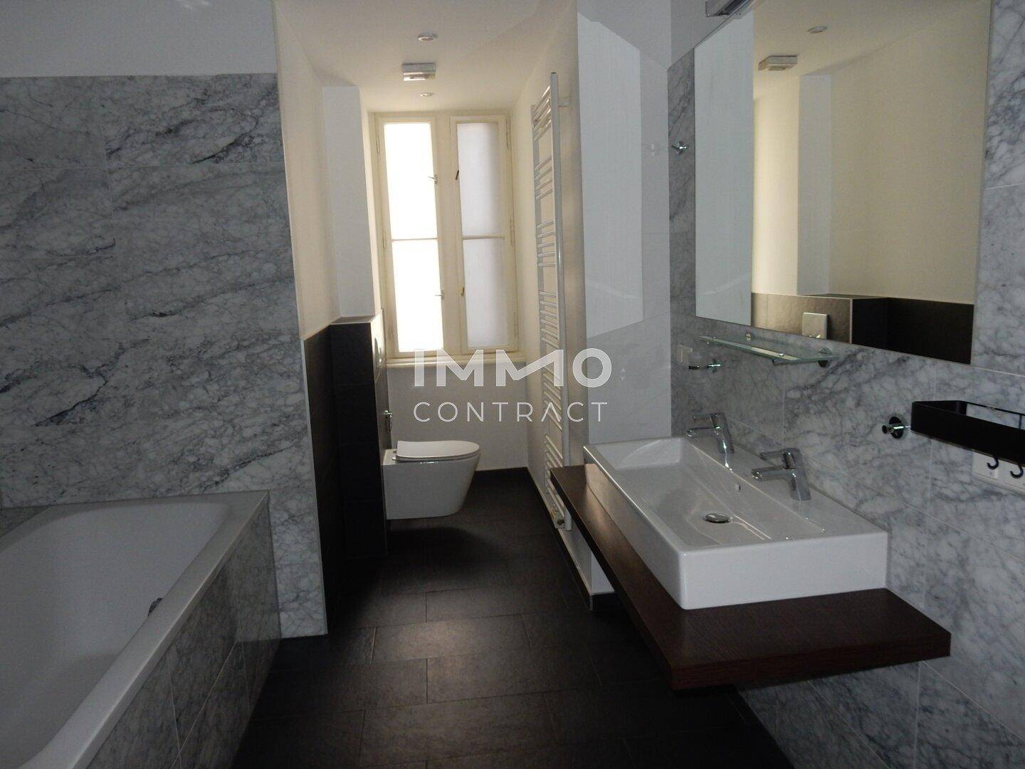 Elegantes Badezimmer mit Marmorfliesen, Badewanne, Toilette, Waschtisch und Fenster.