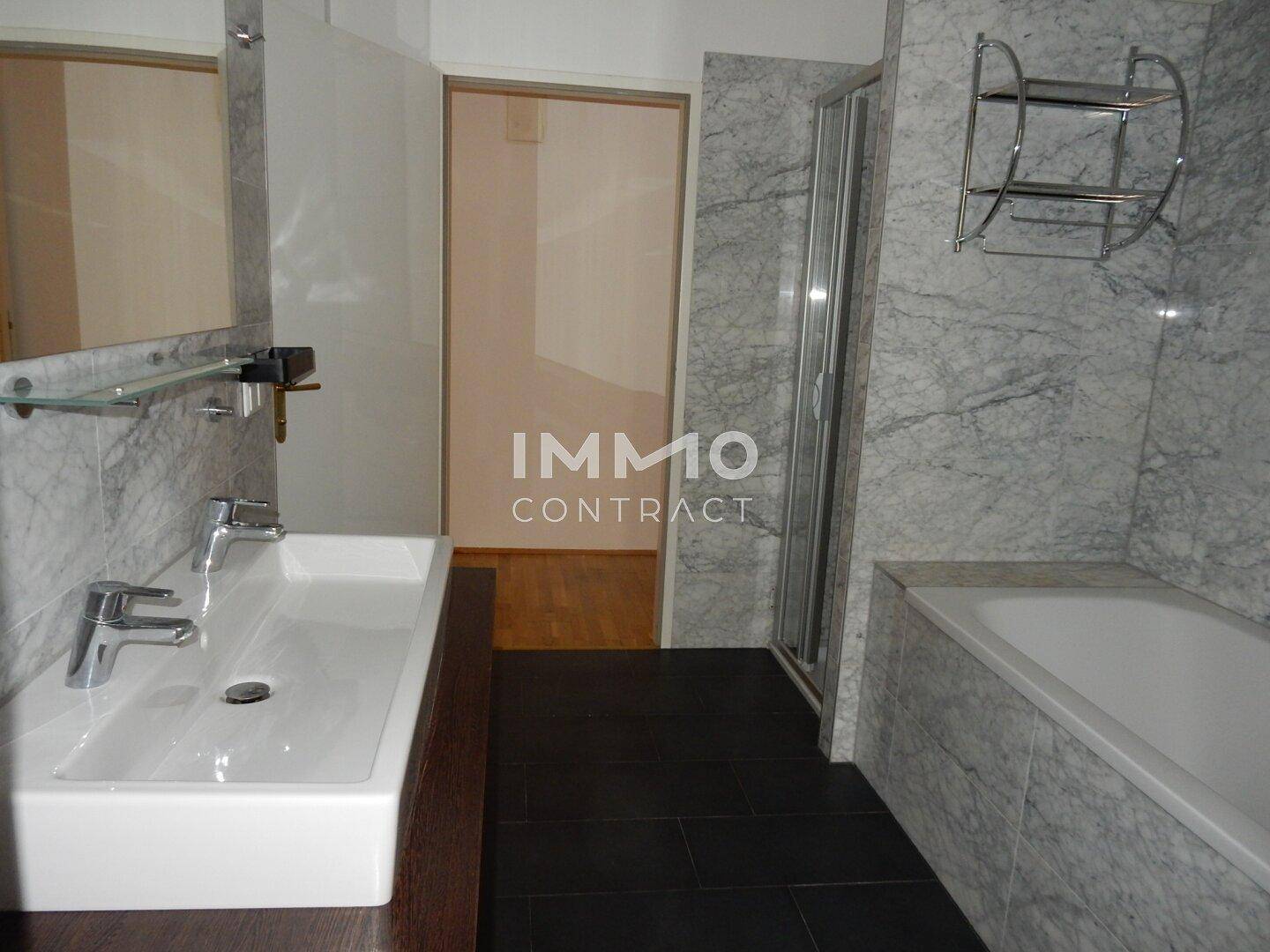 Modernes Badezimmer mit Marmoroptik-Fliesen, Badewanne, Duschkabine und Doppelwaschbecken.