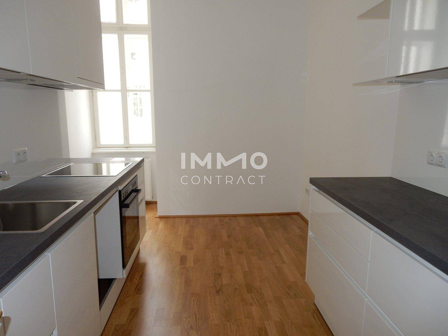 Moderne Küche mit weißen Schränken, dunklen Arbeitsplatten und integrierten Geräten.