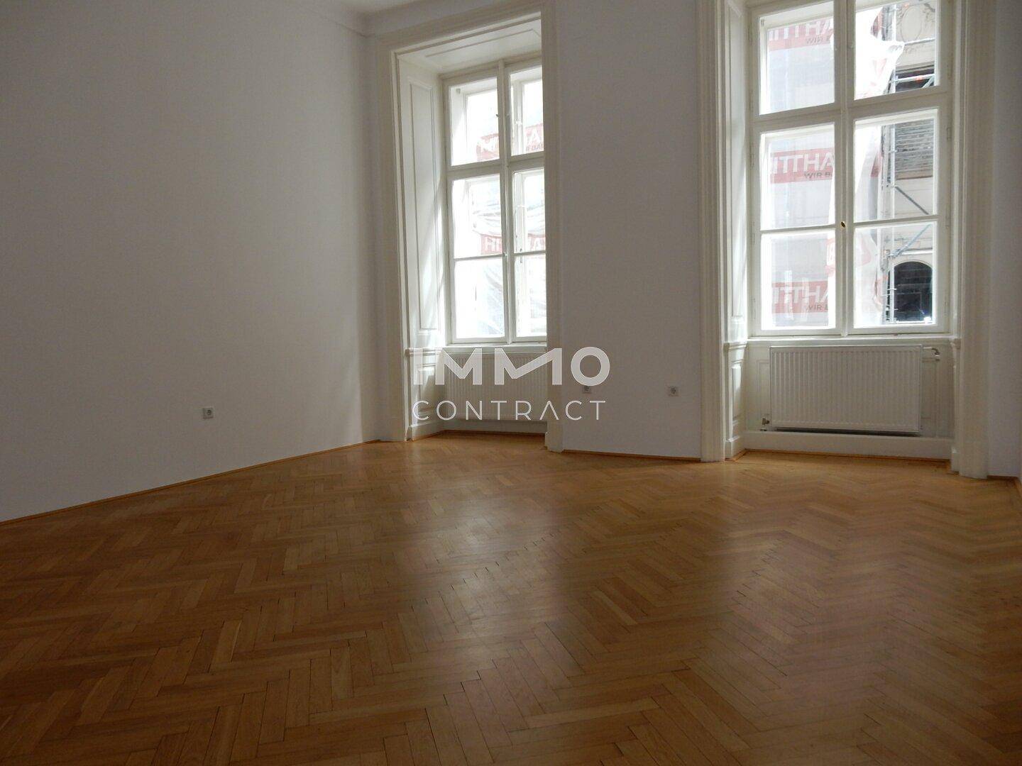 Heller Raum mit elegantem Fischgrätparkett und zwei hohen Fenstern, die viel Licht hereinlassen.