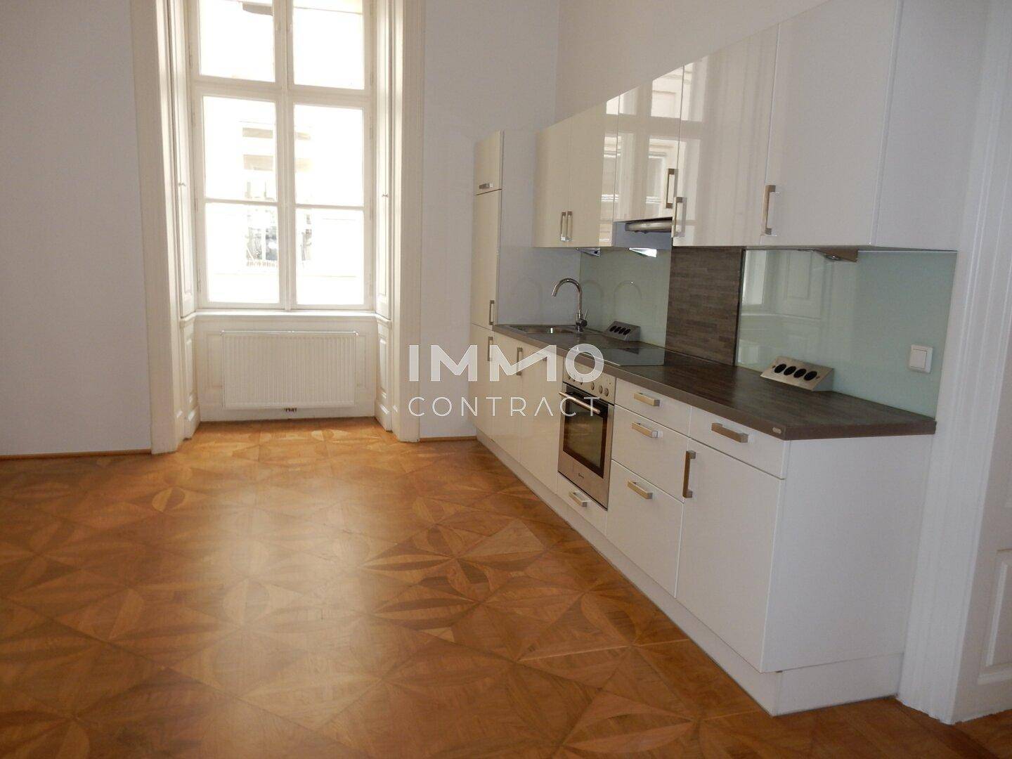 Helle Wohnküche mit modernem Parkettboden, weißer Einbauküche und großem Fenster.