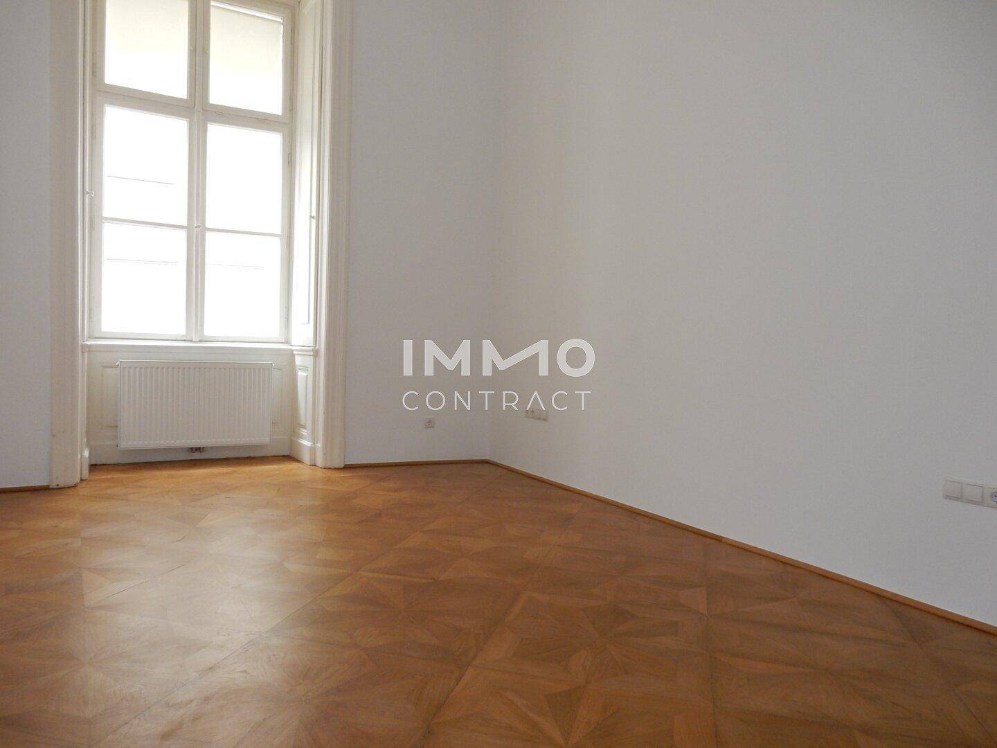 Heller Raum mit elegantem Parkettboden und einem hohen Fenster, das den Raum mit Licht erfüllt.