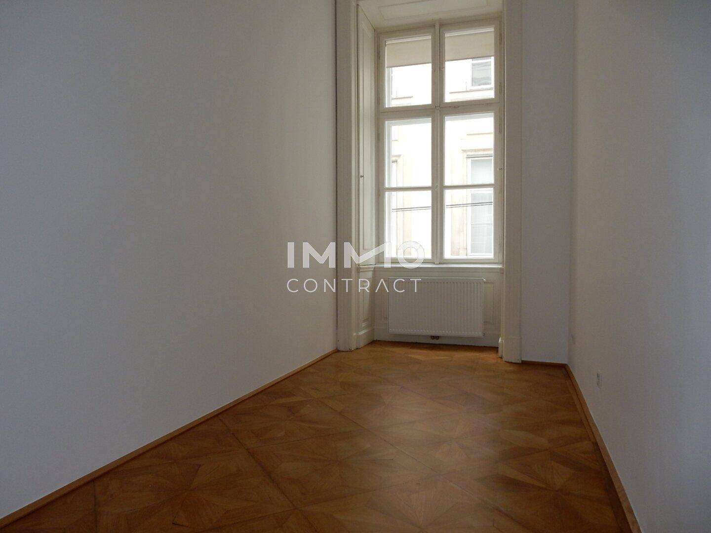 Heller Raum mit dekorativem Parkettboden und einem hohen Fenster, das den Raum gut belichtet.