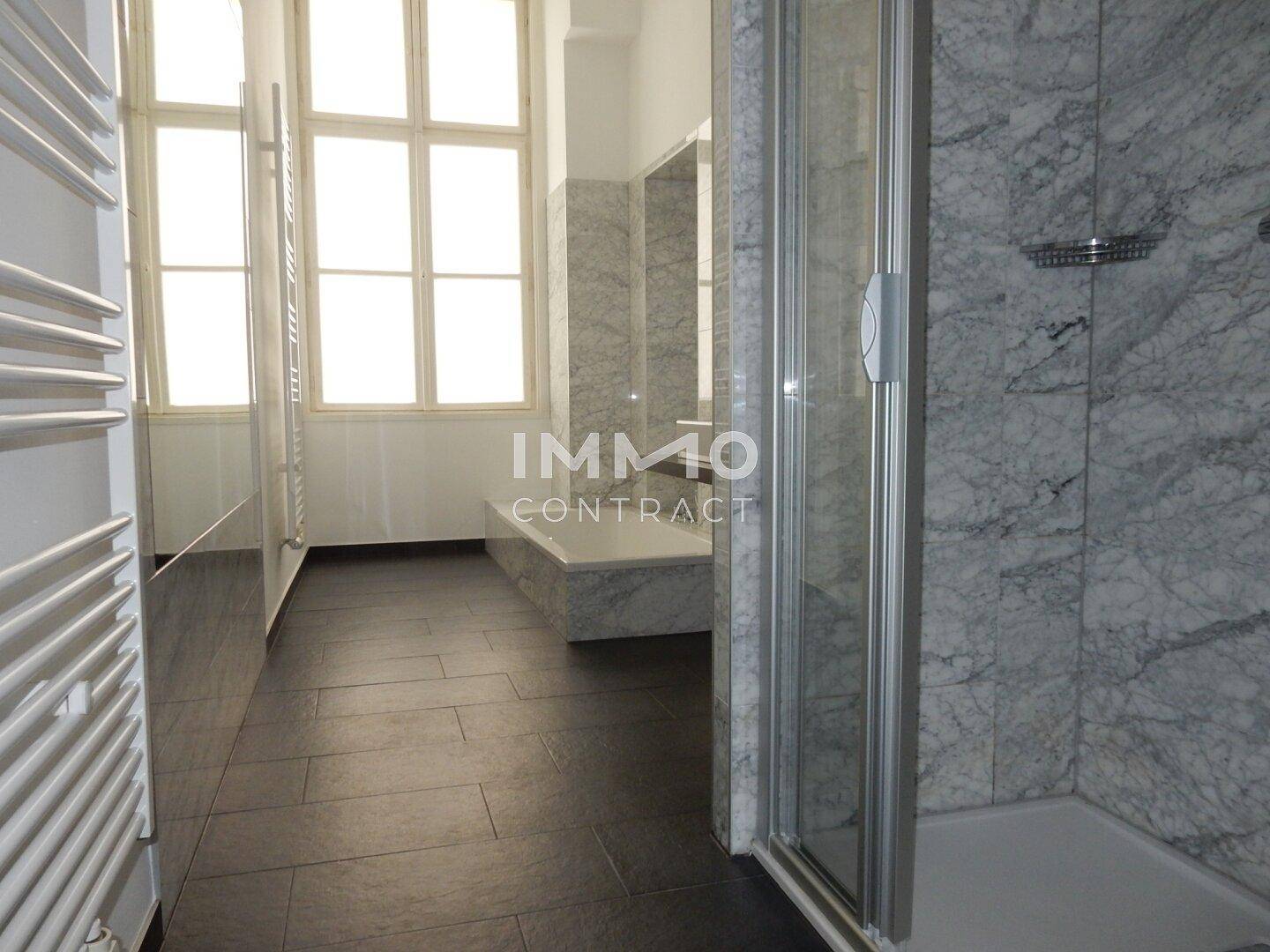 Modernes Badezimmer mit dunklen Fliesen, Marmorwänden, Duschkabine, Badewanne und großem Fenster.