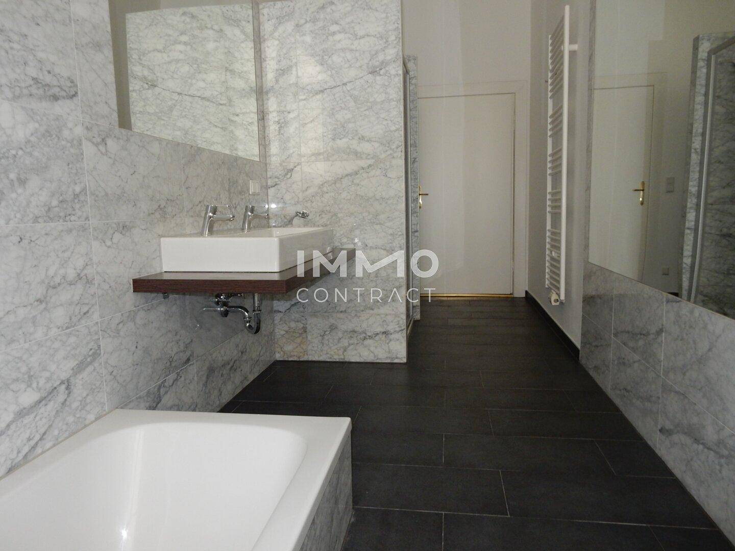 Elegantes Badezimmer mit dunklem Fliesenboden, Marmorwänden, modernem Waschbecken und Badewanne.