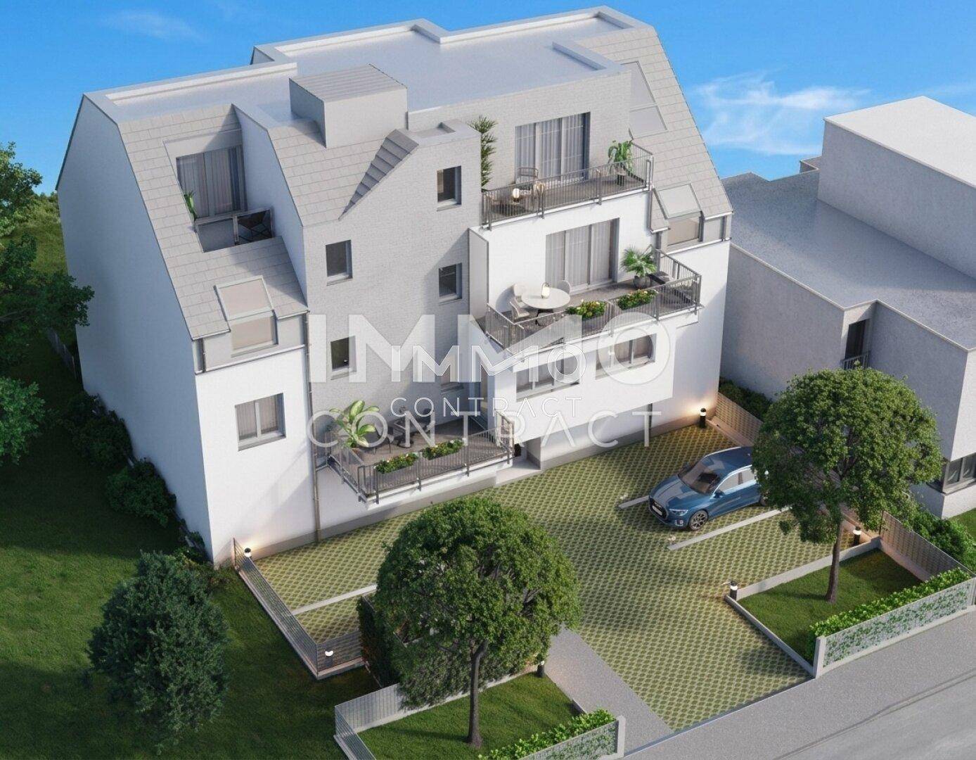Vogelperspektive eines modernen Wohngebäudes mit mehreren Balkonen und Dachschrägen. Eine Parkfläche ist ebenfalls sichtbar.
