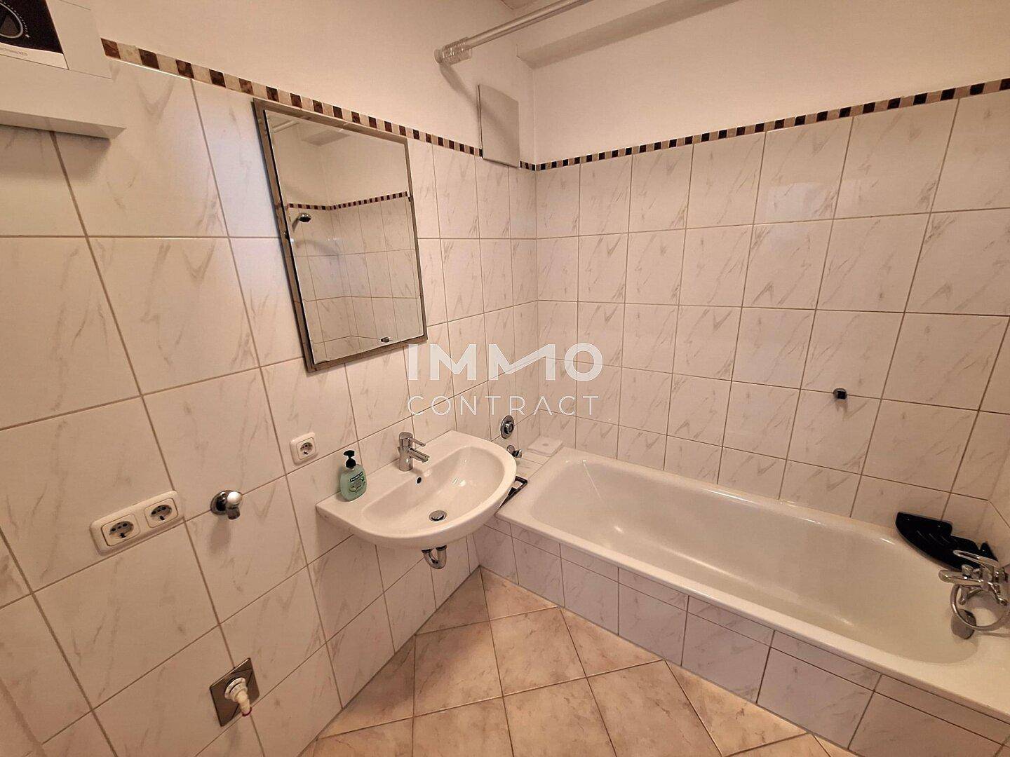 Gefliestes Badezimmer mit Badewanne, Waschbecken und Spiegel.
