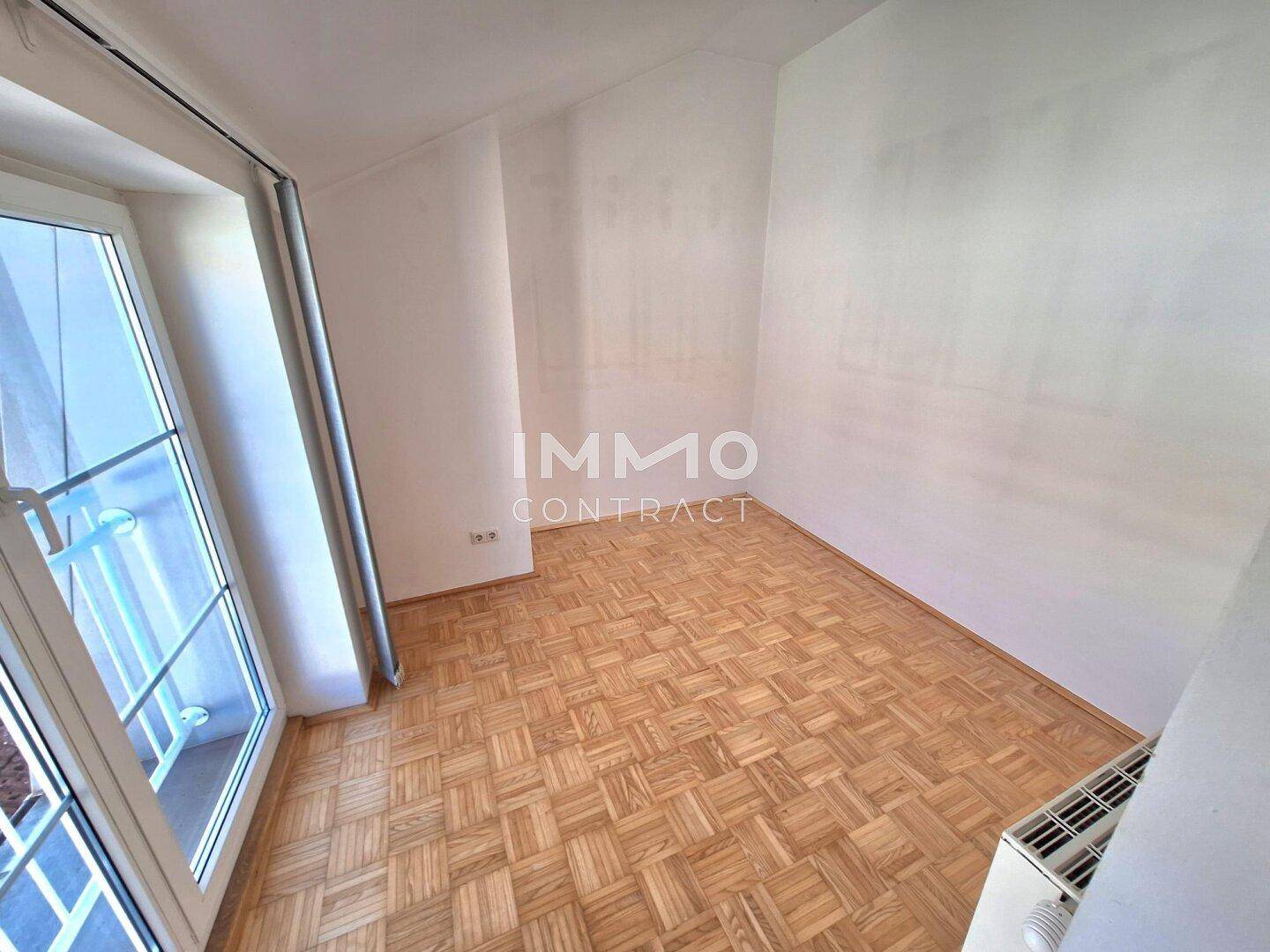 Leeres Schlafzimmer mit Parkettboden und einem französischen Balkon.