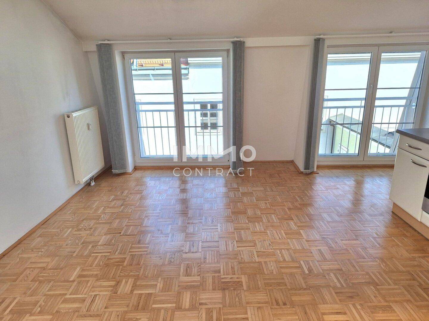 Heller, leerer Wohnbereich mit Parkettboden und zwei französischen Balkonen.
