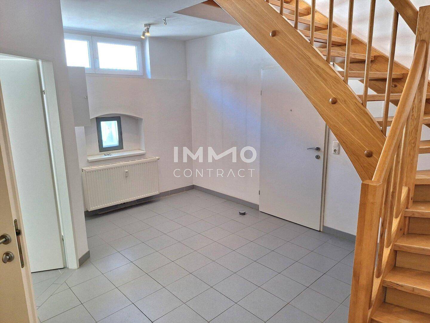 Eingangsbereich mit Holztreppe, Fliesenboden und kleinem Fenster.